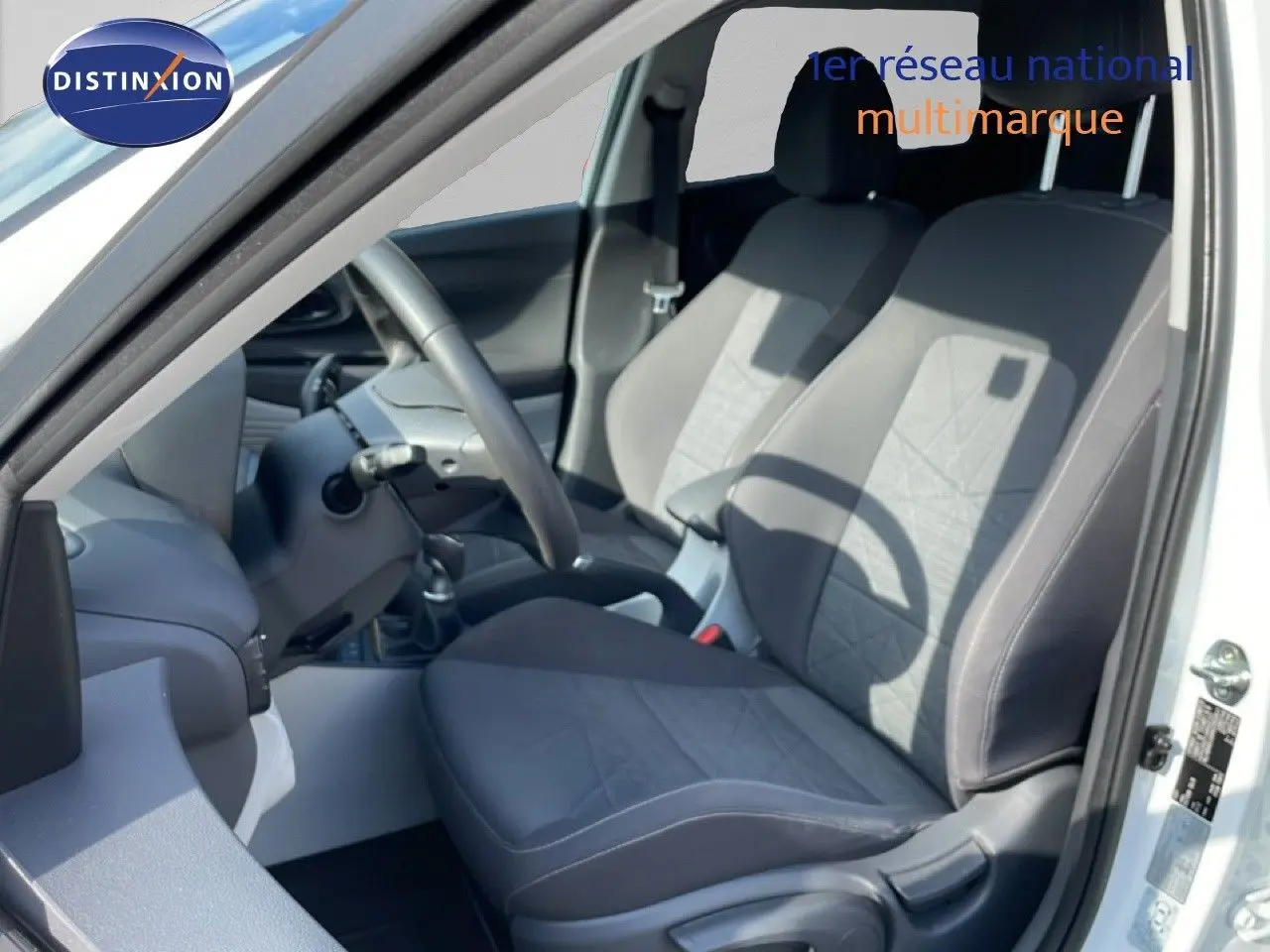 Vue intérieure côté conducteur du Hyundai Bayon blanc polaire, mettant en valeur les sièges tissu gris et le volant multifonction.