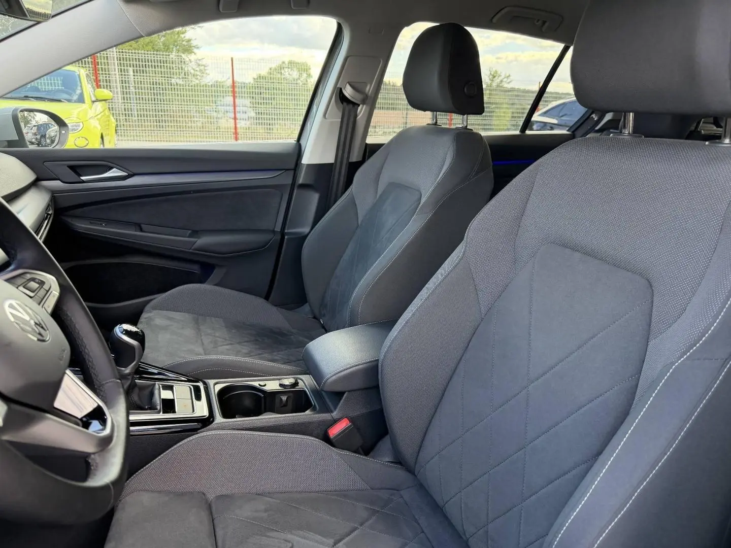 Vue intérieure côté avant droit de la Volkswagen Golf 1.5 TSI Style 2024 avec sièges sport gris et accoudoir central.