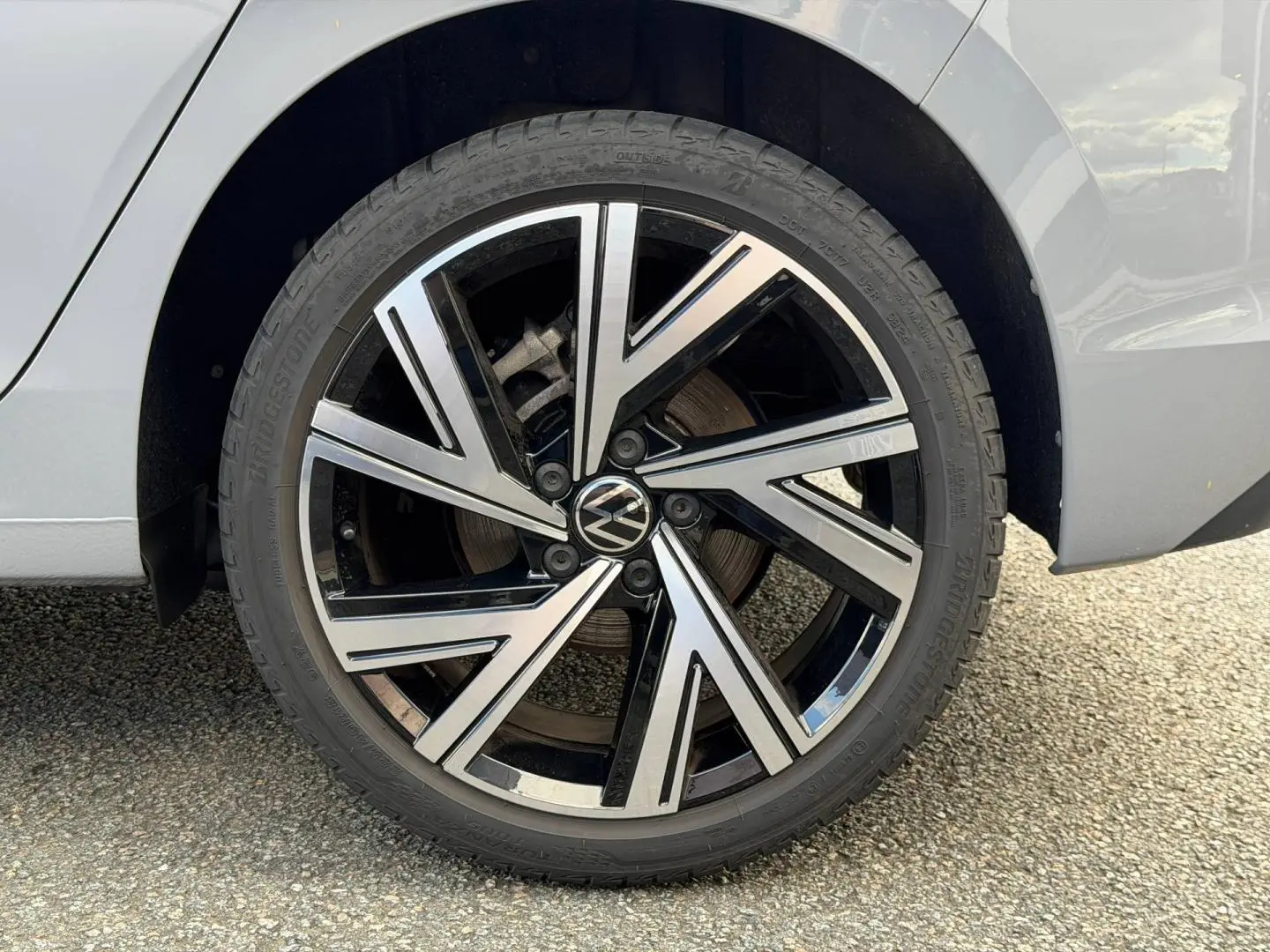 Gros plan sur la roue arrière droite de la Volkswagen Golf 2024 gris lunaire avec jante alliage noir et argentée.