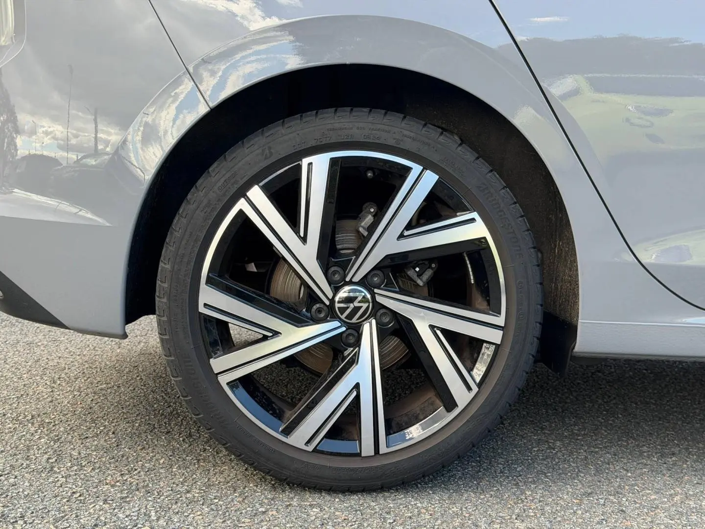 Gros plan sur la roue arrière droite d'une Volkswagen Golf gris lunaire avec jante alu bicolore moderne.