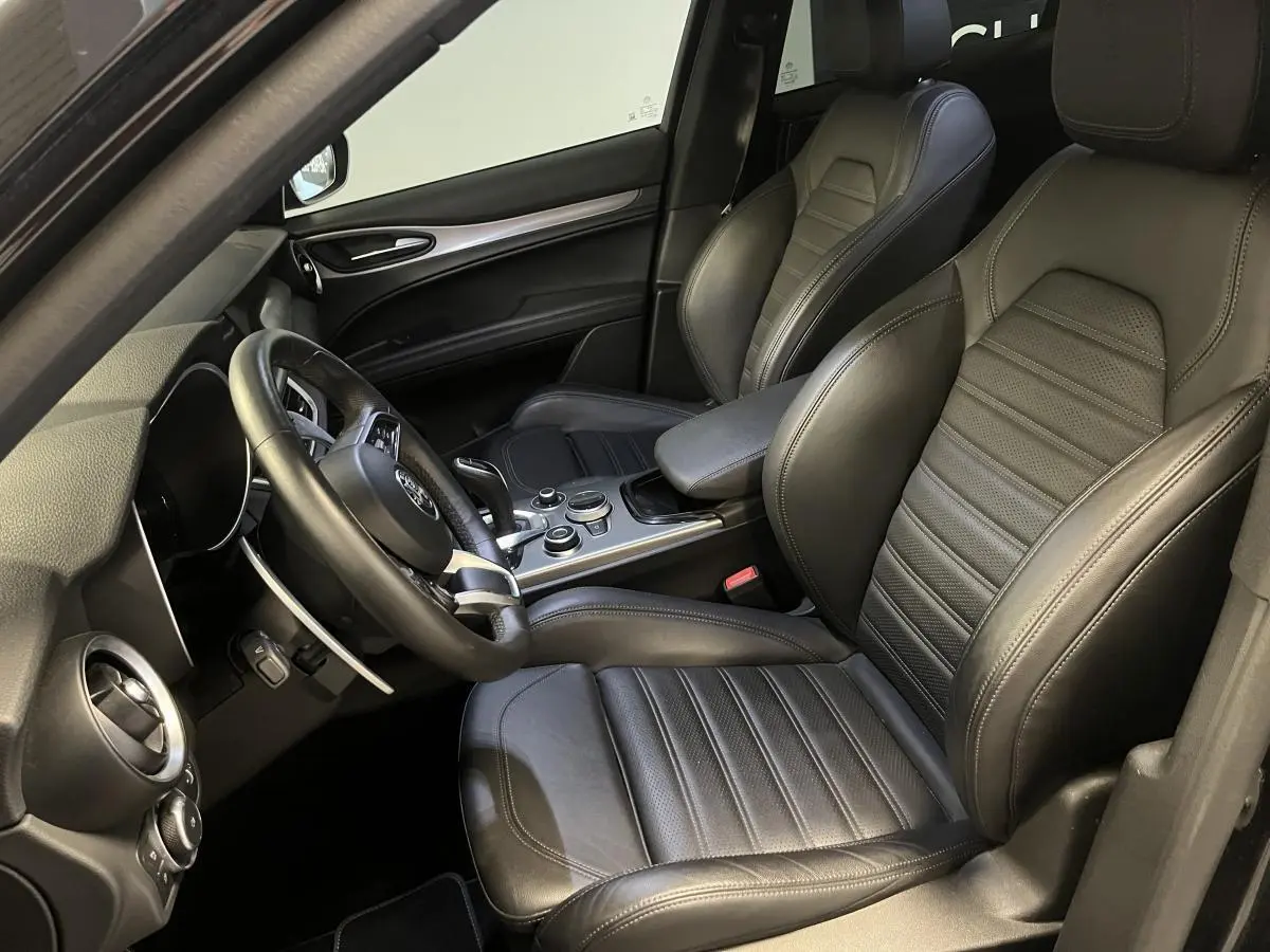 Intérieur noir de l'Alfa Romeo Stelvio Veloce 2024, vue côté conducteur avec sièges sport en cuir et console centrale.