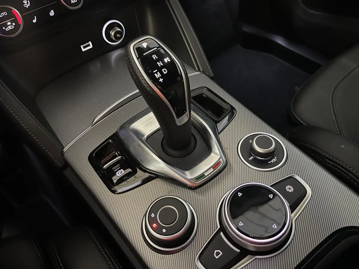 Gros plan sur la console centrale de l'Alfa Romeo Stelvio Veloce 2024 avec levier de vitesse automatique et commandes en finition carbone.