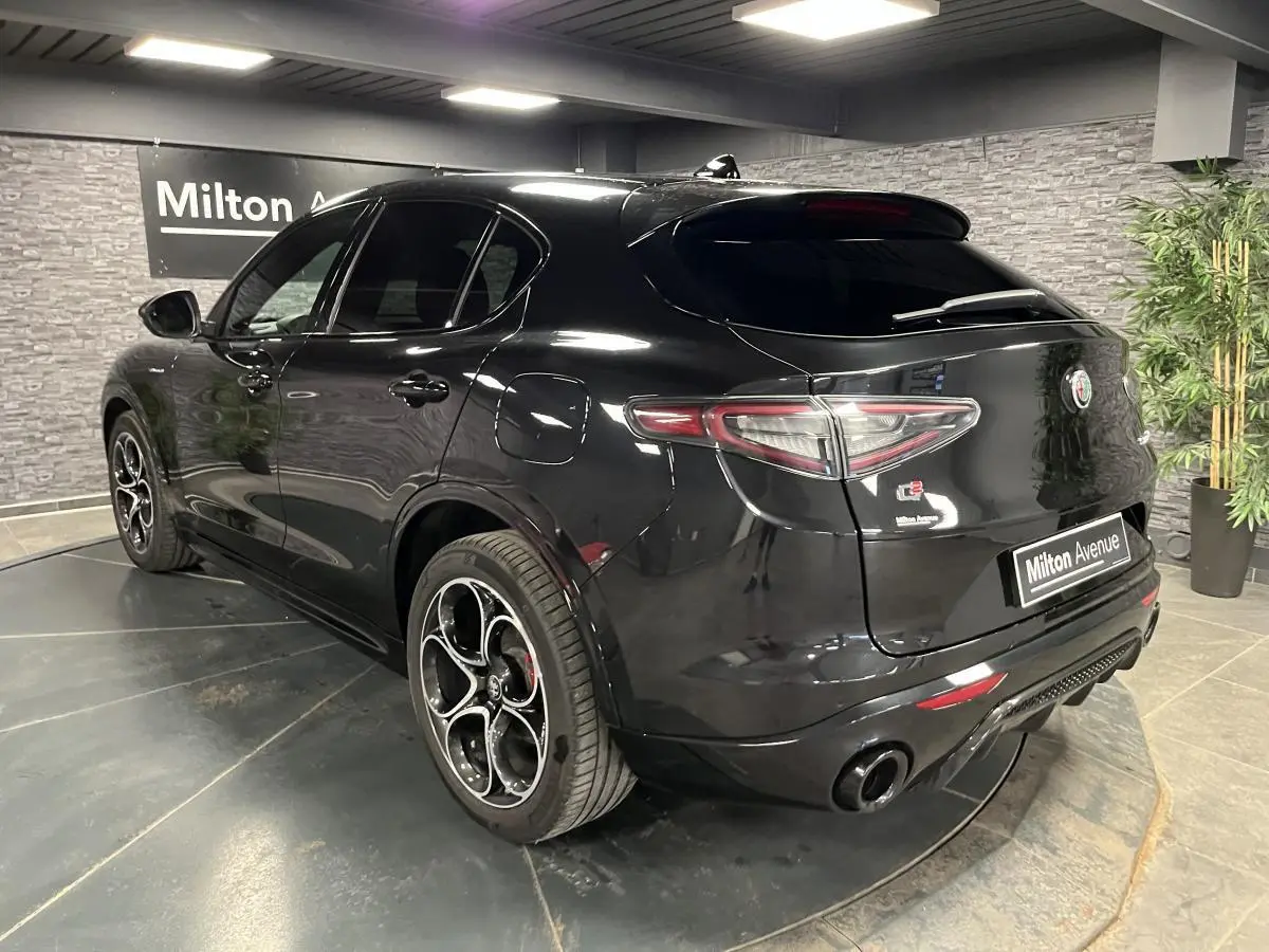 Vue 3/4 arrière côté gauche d'un Alfa Romeo Stelvio Veloce noir métallisé avec jantes 20 pouces et double sortie d'échappement noire.