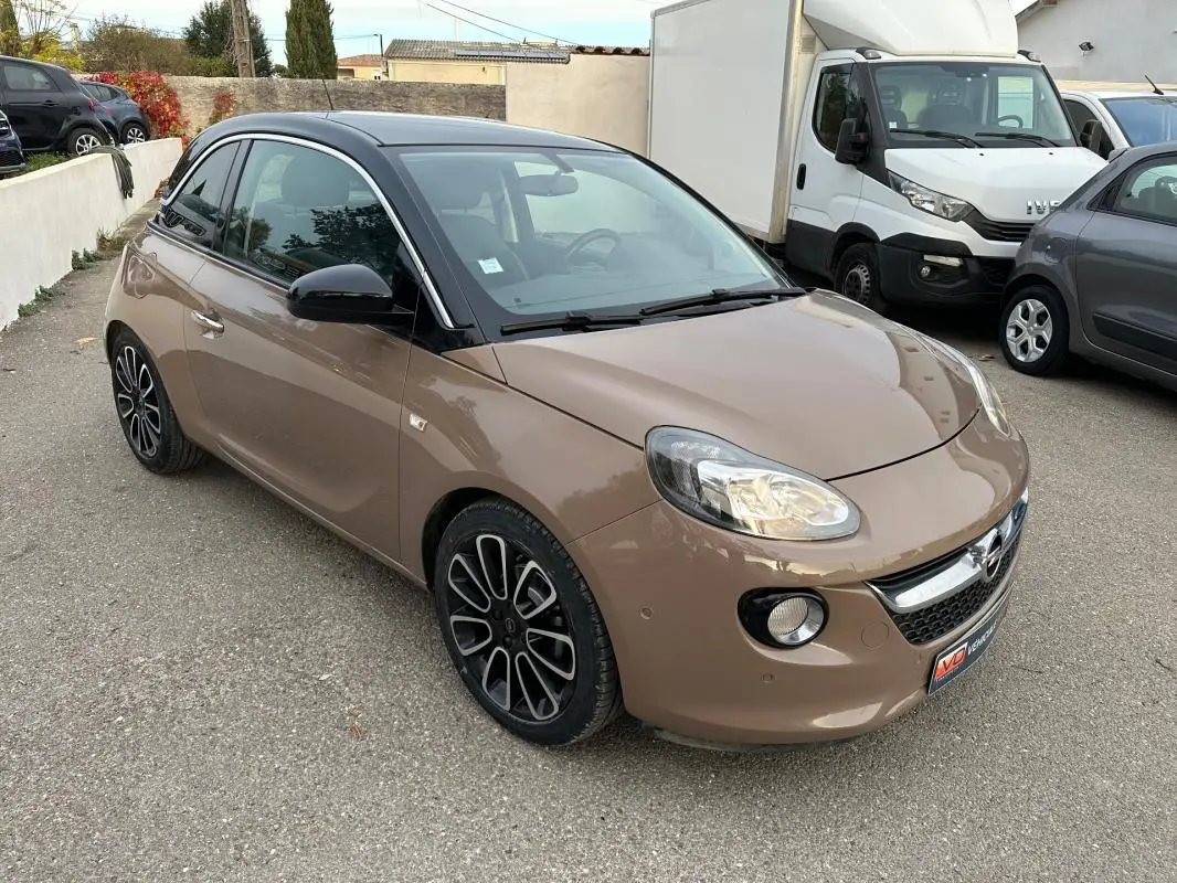 Opel Adam marron vue 3/4 avant droit, toit noir, jantes alliage 16 pouces et phares allumés sur parking.