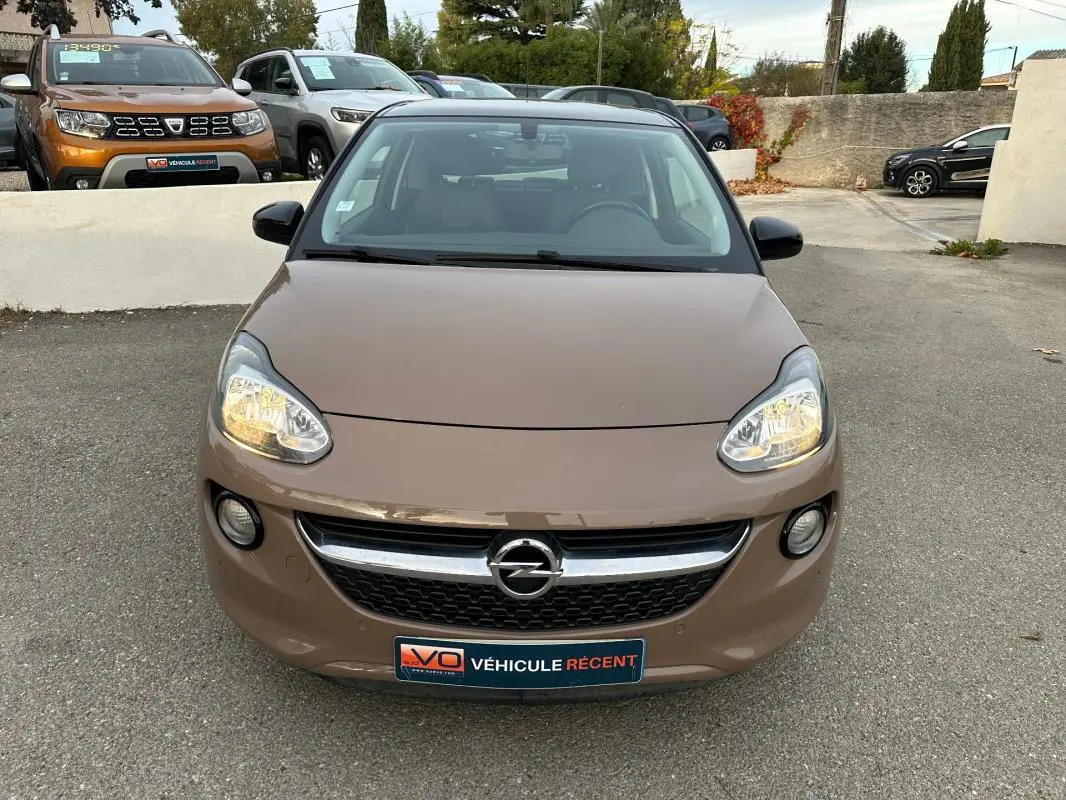 Vue avant d'une Opel Adam marron 2016 avec phares allumés et calandre chromée sur parking extérieur.