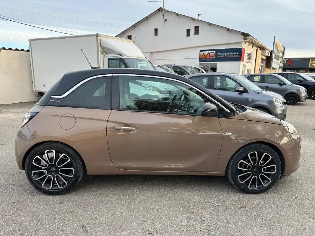 Profil côté gauche d'une Opel Adam marron avec toit noir et jantes alliage 16 pouces sur un parking extérieur.