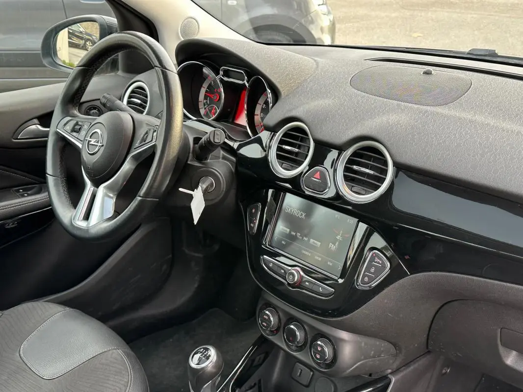 Intérieur de l'Opel Adam 2016 vu côté conducteur, volant cuir multifonctions et écran tactile central noir brillant.
