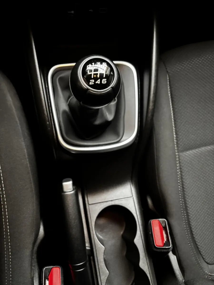 Gros plan sur le levier de vitesses manuel noir et la console centrale entre les sièges avant gris foncé du Fiat Tipo blanc.