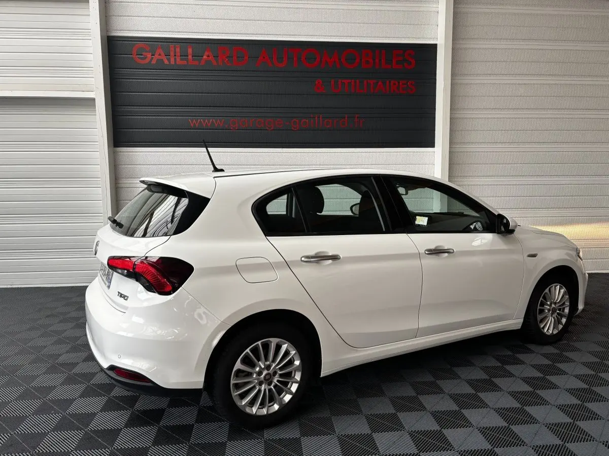 Vue 3/4 arrière droite d'une Fiat Tipo blanche 5 portes garée en intérieur avec jantes alliage et feux arrière rouges.