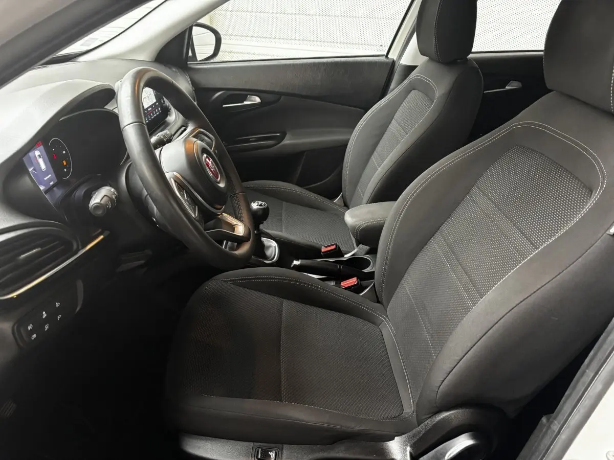 Intérieur avant droit du Fiat Tipo 1.6 MultiJet 2021, sièges noirs, volant cuir multifonctions et levier de vitesses manuel.