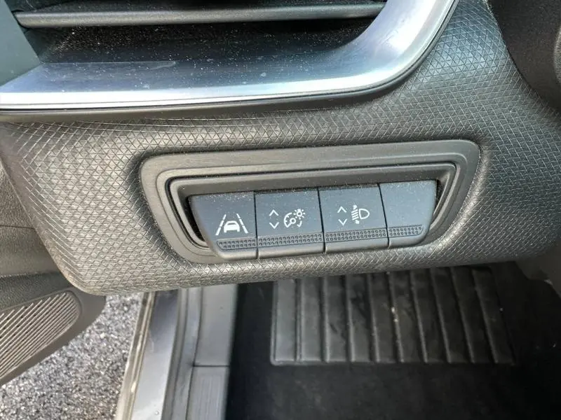 Gros plan sur les commandes noires de réglage d'assistance et d'éclairage dans une Renault Clio gris 2023, côté conducteur.