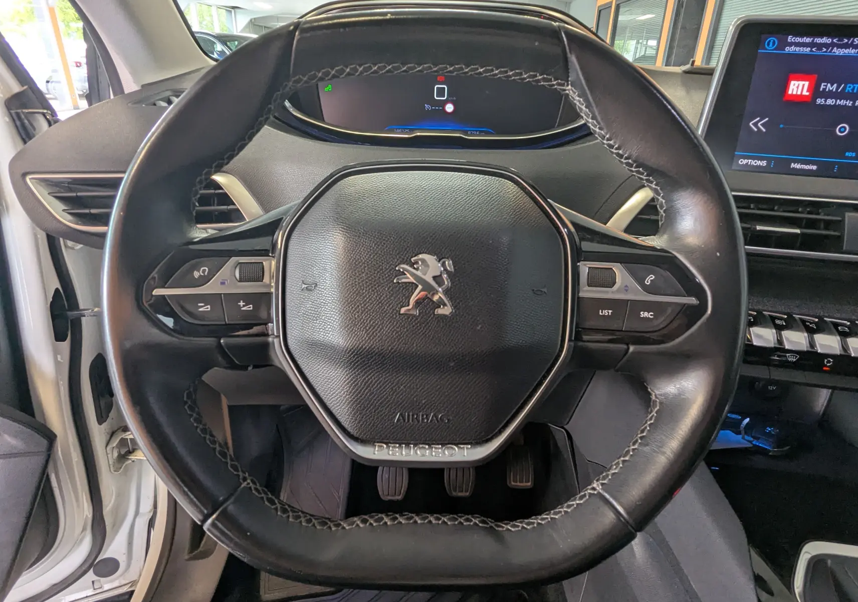 Vue rapprochée du volant cuir noir du Peugeot 3008 HDi 130 Allure 2018, avec tableau de bord digital et écran central visible.