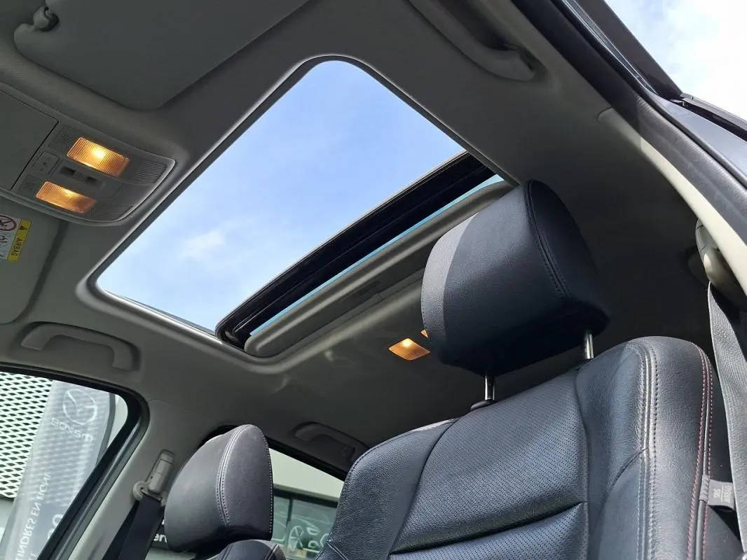 Vue intérieure du toit ouvrant électrique et siège avant cuir noir du Mazda CX-5 gris 2015 avec ciel bleu visible.