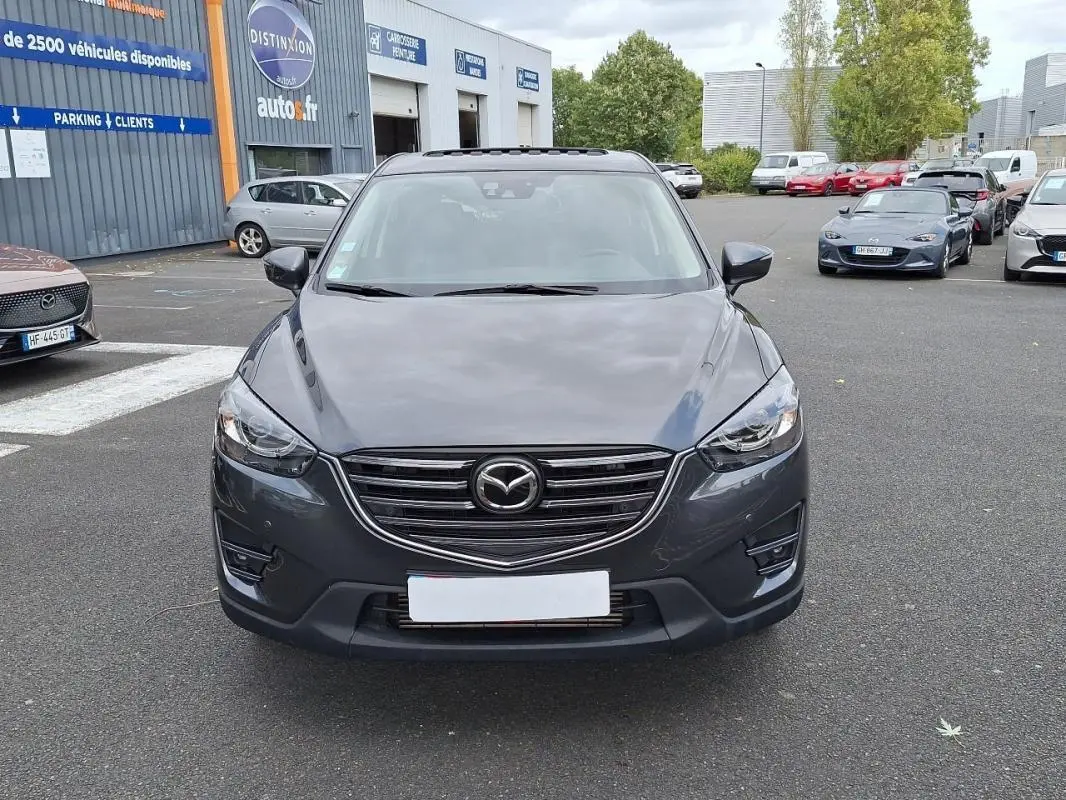 Vue frontale d'un Mazda CX-5 gris 2015 avec calandre chromée et phares LED sur parking extérieur.