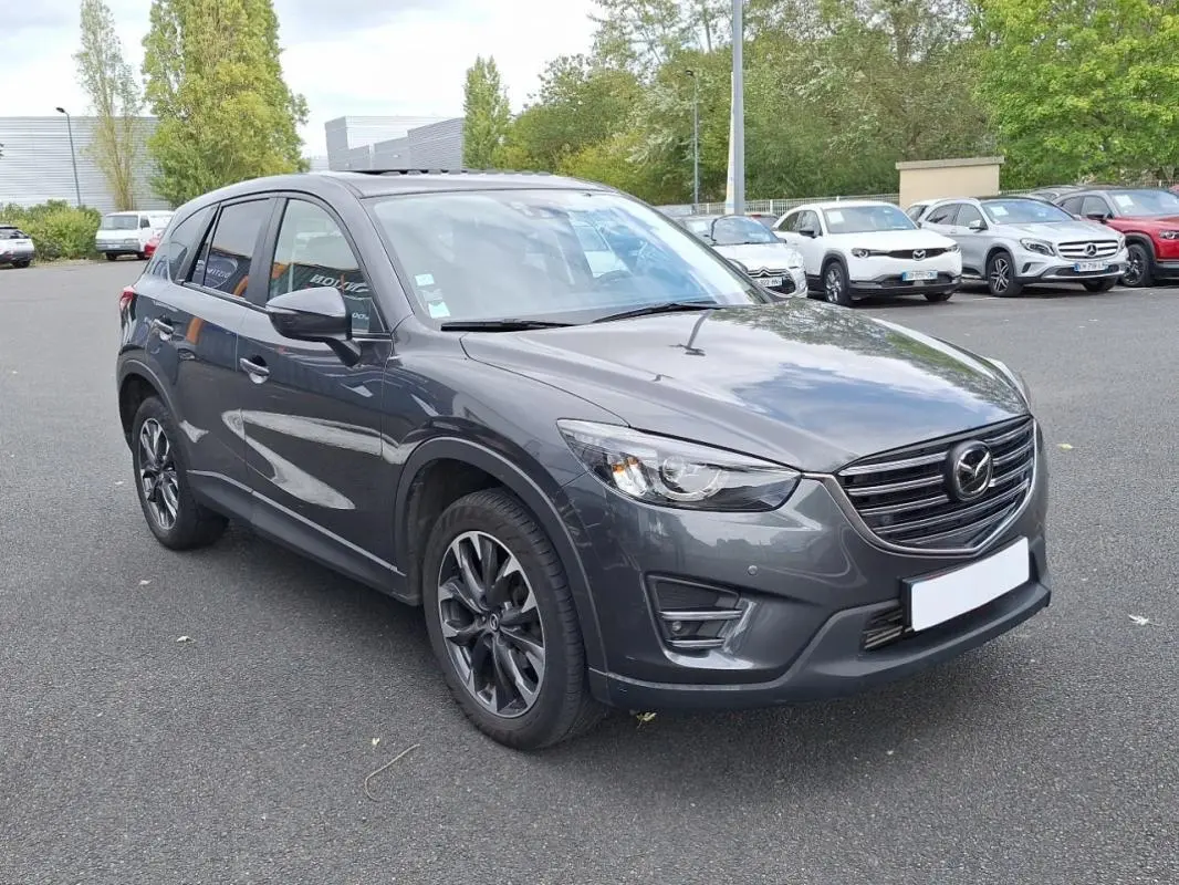 Vue 3/4 avant droit d'un Mazda CX-5 gris métallisé avec jantes alliage et vitres surteintées sur parking extérieur.