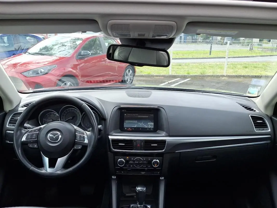 Vue intérieure avant du tableau de bord et volant cuir multifonctions de la Mazda CX-5 gris 2015 avec écran tactile GPS intégré.