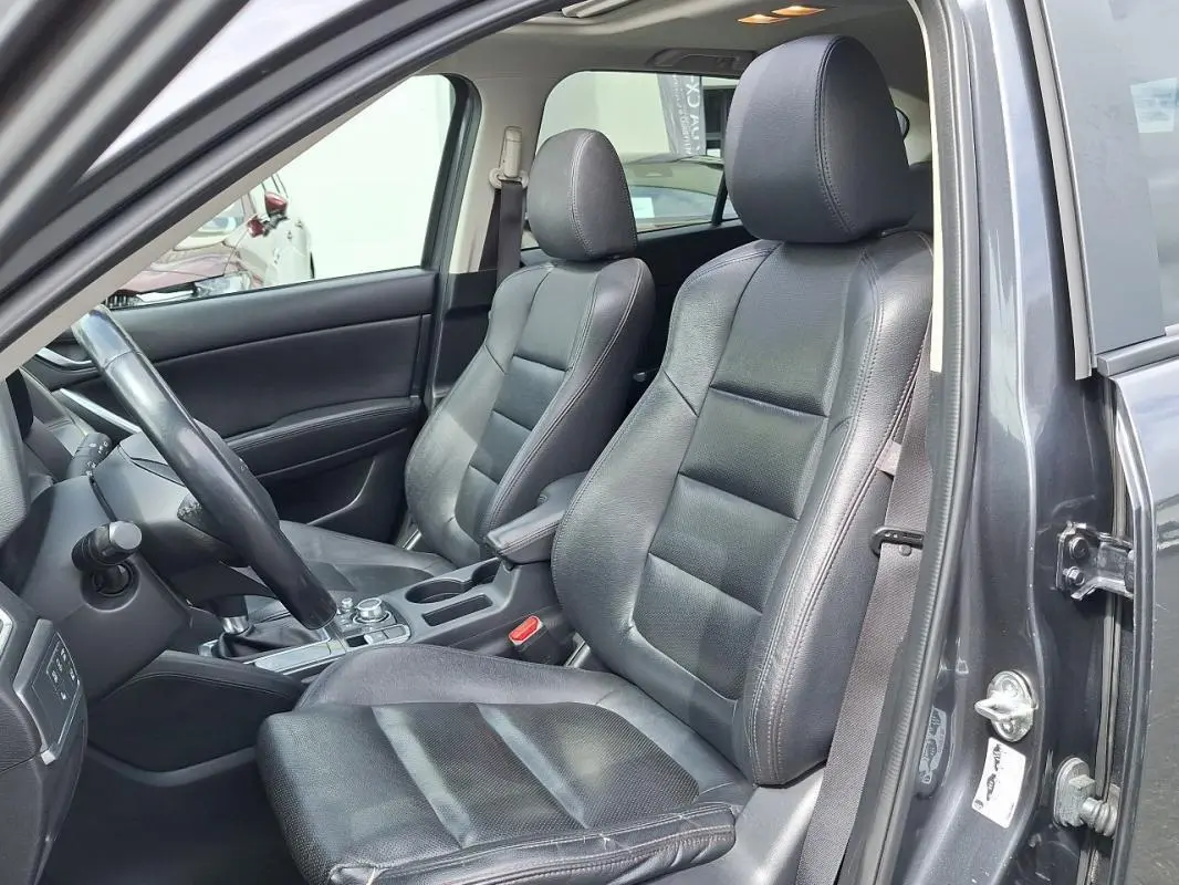 Vue intérieure côté conducteur du Mazda CX-5 gris 2015, sièges en cuir noir et volant multifonctions visible.