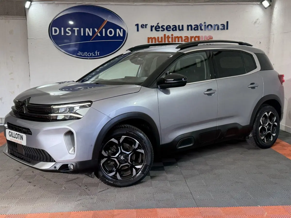 Citroën C5 Aircross gris clair en 3/4 avant droit, avec jantes noires et toit noir contrasté en intérieur showroom.