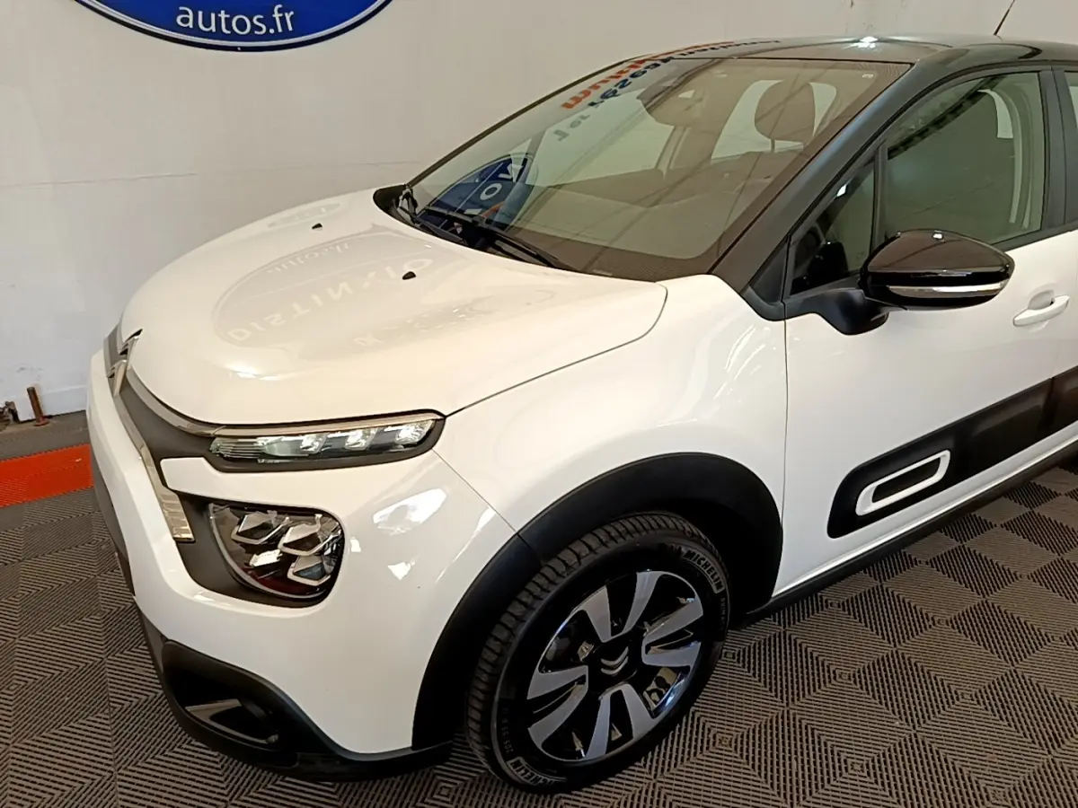 Vue 3/4 avant droite d'une Citroën C3 blanche avec protections latérales noires et jantes alliage distinctives.