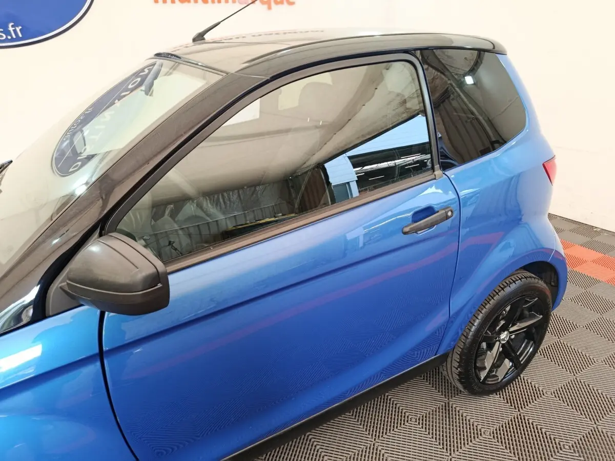 Vue côté gauche en 3/4 arrière d'une Aixam Ambition 0.5 City Sport bleu avec rétroviseur conducteur noir.