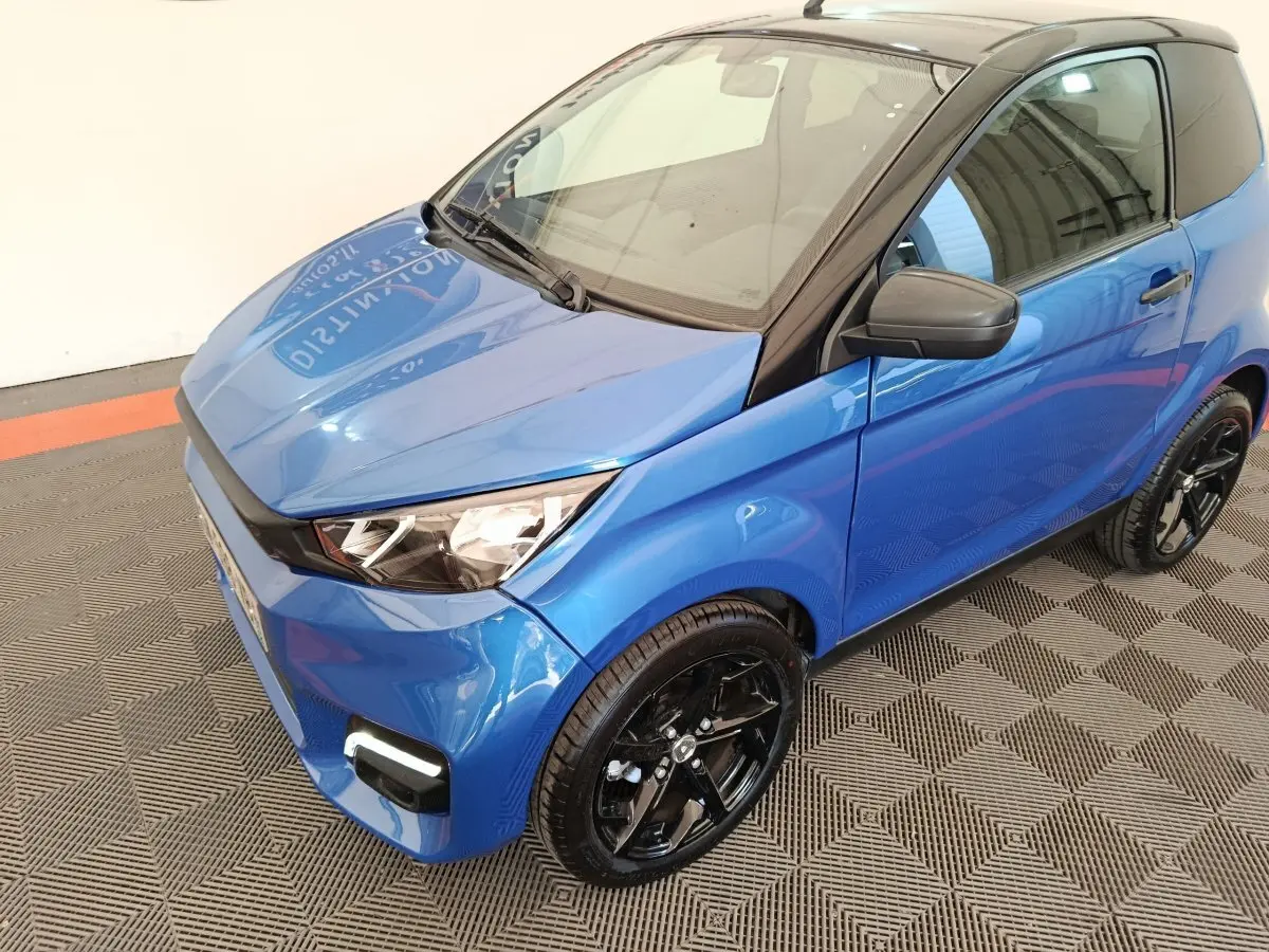 Vue 3/4 avant droit d'une Aixam Ambition 0.5 City Sport 2024 bleu avec rétroviseur côté conducteur noir et jantes noires.