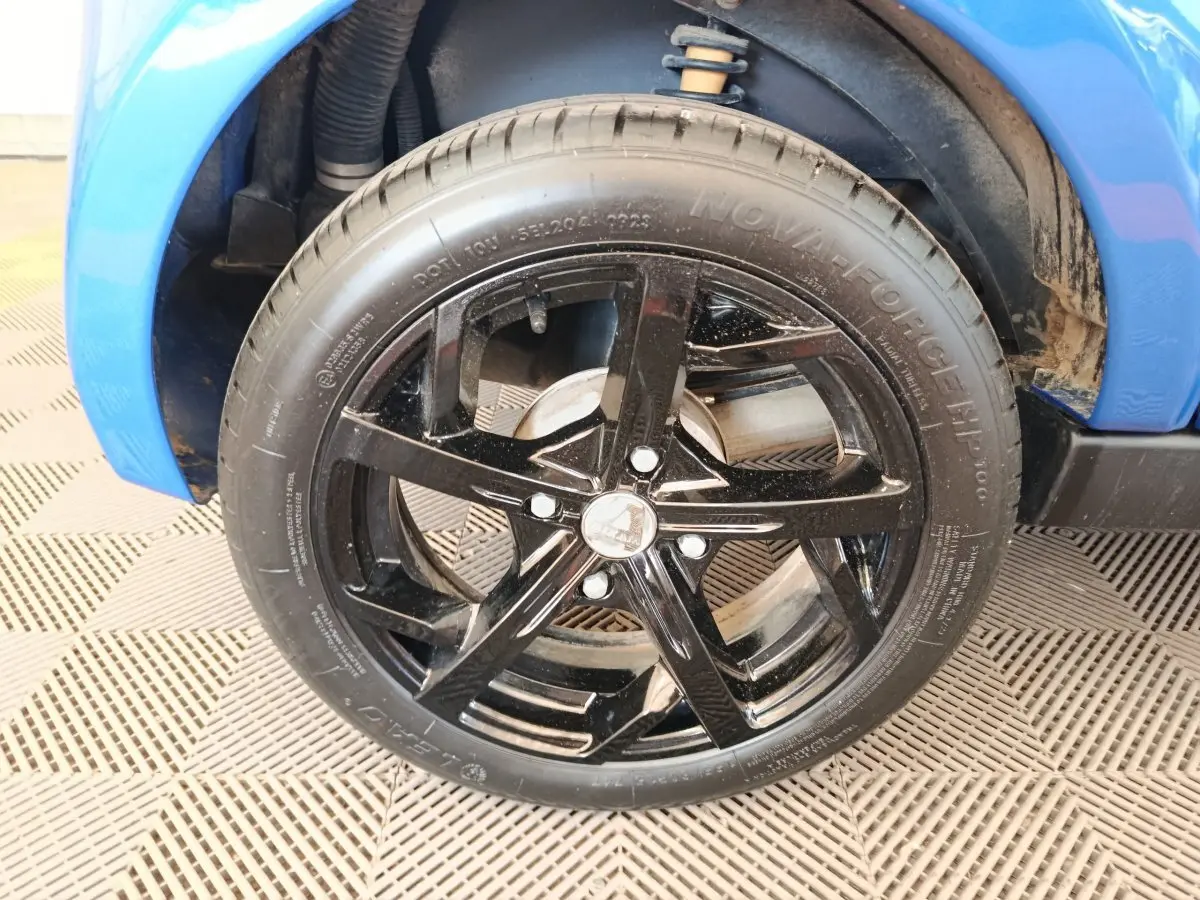 Gros plan sur la roue avant droite noire avec jante étoile du véhicule bleu Aixam Ambition 0.5 City Sport 2024.