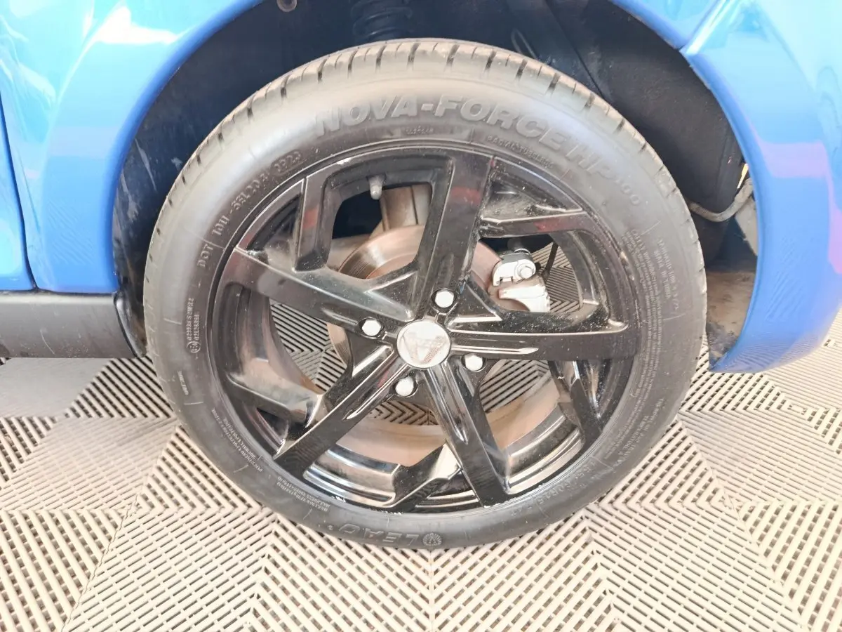 Gros plan sur la roue avant droite noire d’une Aixam Ambition 0.5 City Sport bleu 2024.