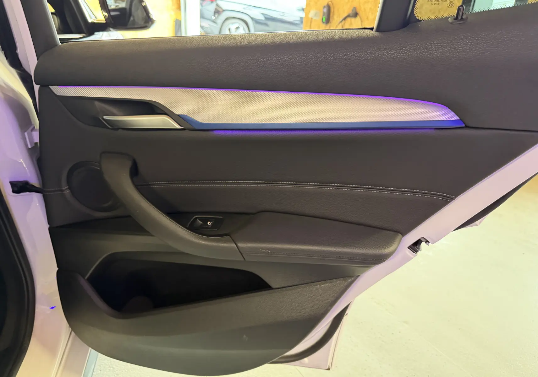 Vue intérieure de la porte arrière droite d'une BMW X2 blanche avec éclairage d'ambiance violet et garniture noire.