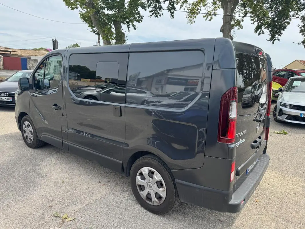 Vue 3/4 arrière droite d’un Renault Trafic Fourgon gris foncé avec porte latérale et vitres surteintées.