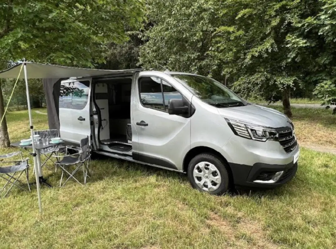 Vue 3/4 avant droit d'un Renault Trafic Fourgon gris foncé avec porte latérale ouverte et auvent déployé.