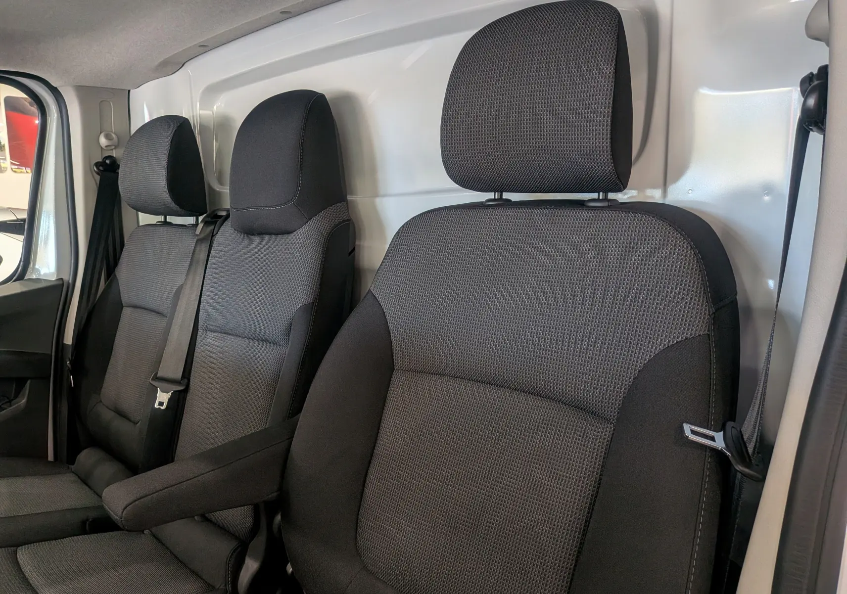 Vue intérieure des sièges avant en tissu gris foncé du Renault Trafic Fourgon blanc glacier, version L1H1 2025.