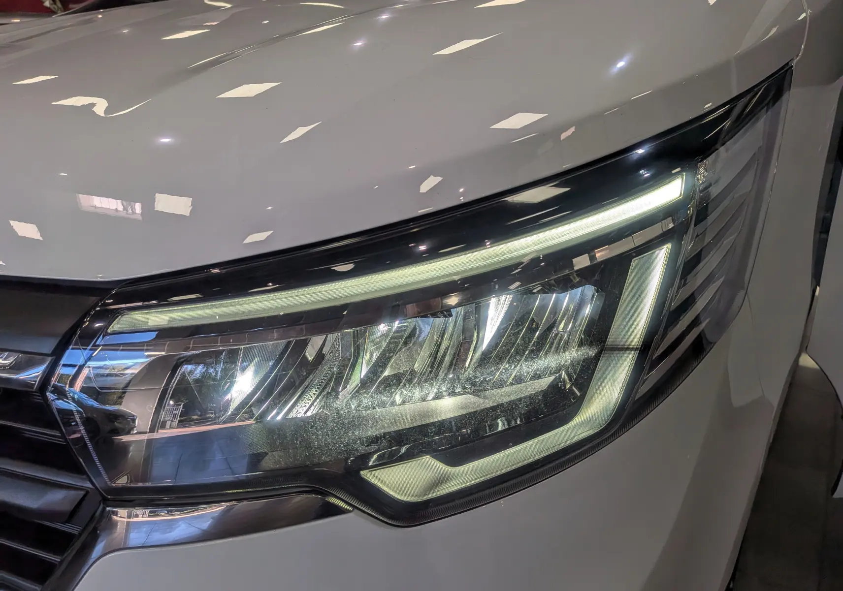 Gros plan sur le phare avant droit du Renault Trafic Fourgon blanc glacier 2025, éclairage LED distinctif visible.