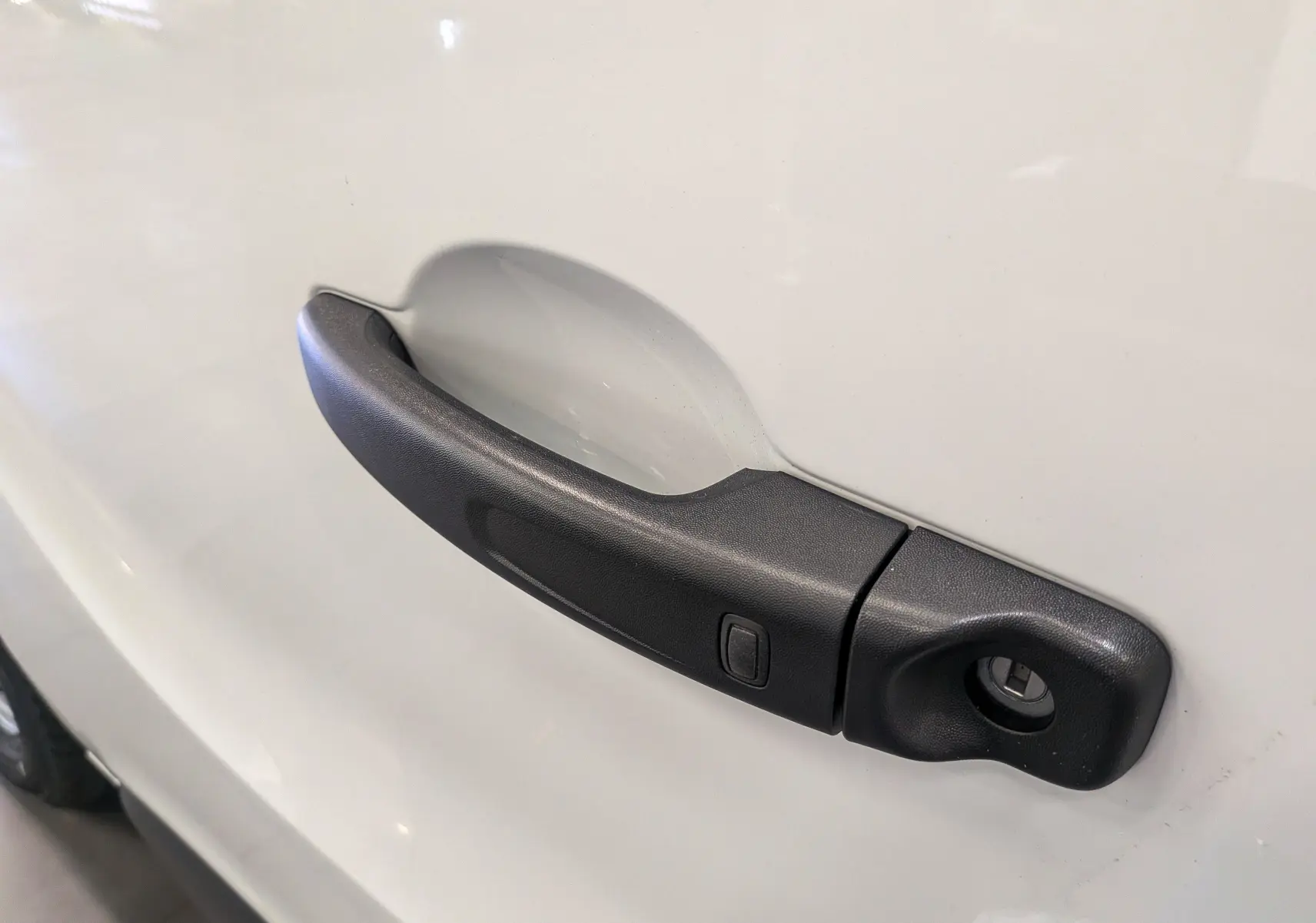 Poignée de porte noire en gros plan sur la portière blanche glacée d'un Renault Trafic Fourgon L1H1 2025.