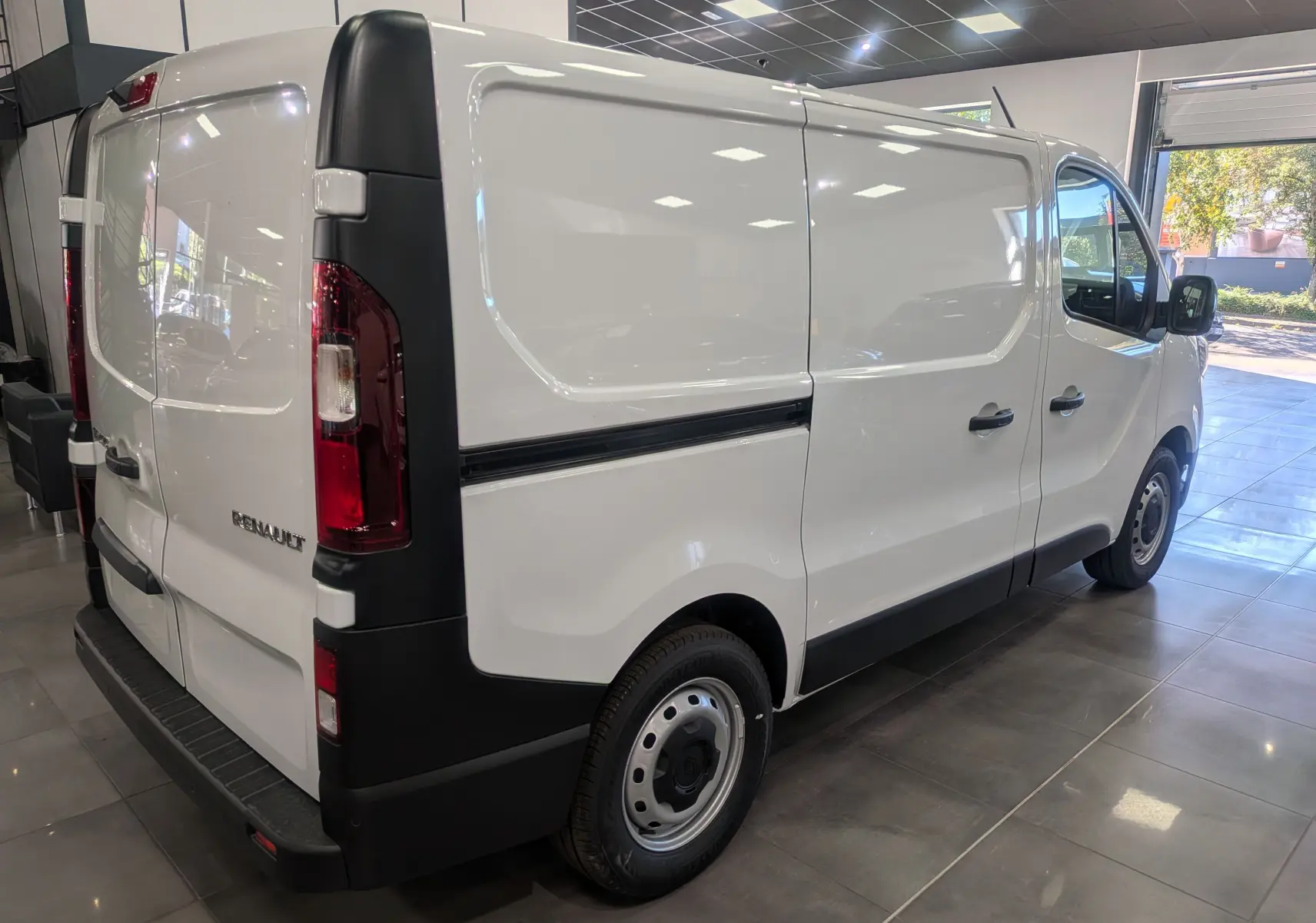 Renault Trafic Fourgon blanc glacier vu en 3/4 arrière droit dans un showroom lumineux avec portes arrière fermées.