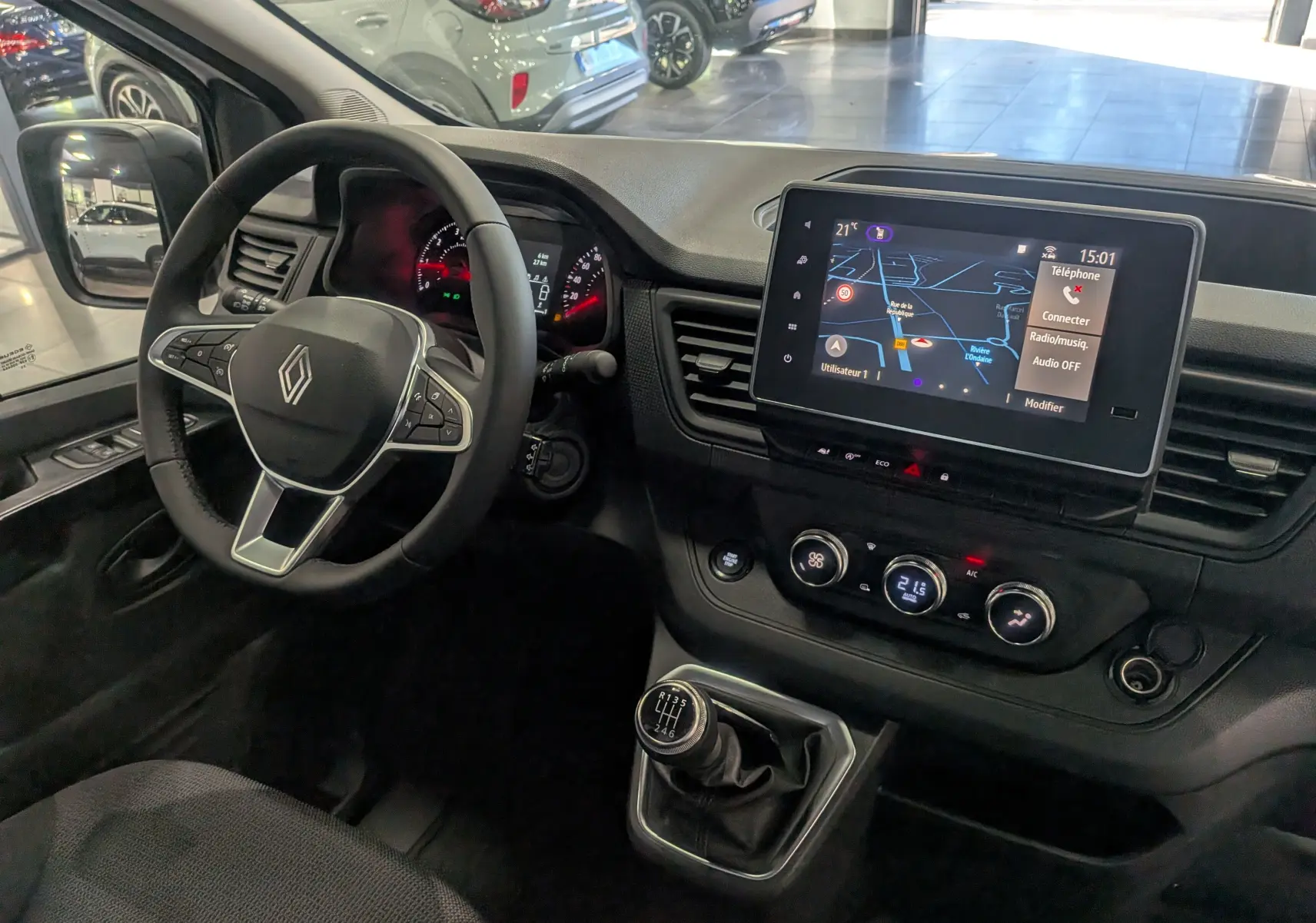 Vue intérieure côté conducteur du Renault Trafic Fourgon L1H1 2025, tableau de bord noir avec écran tactile et levier de vitesses manuel.