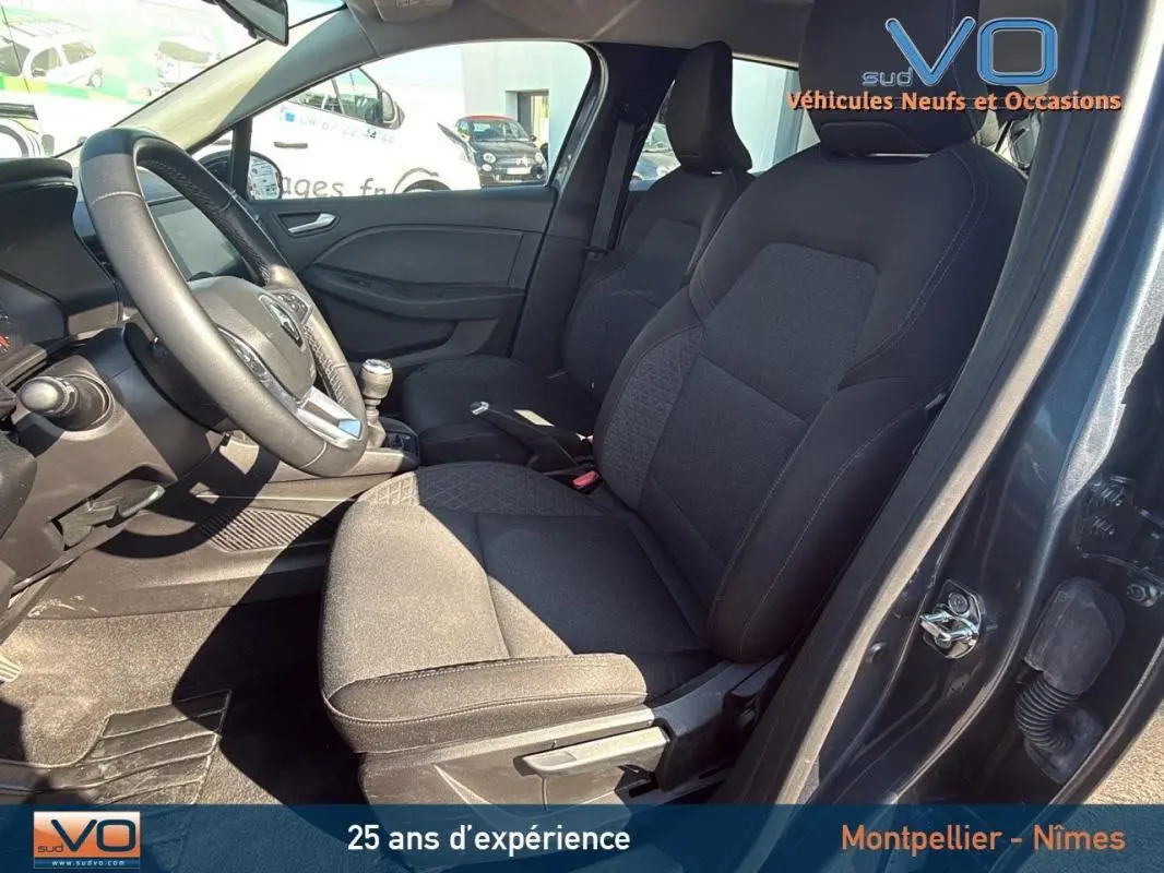 Intérieur avant droit de la Renault Clio gris 2022 montrant sièges tissu noirs et volant avec levier de vitesses manuel.