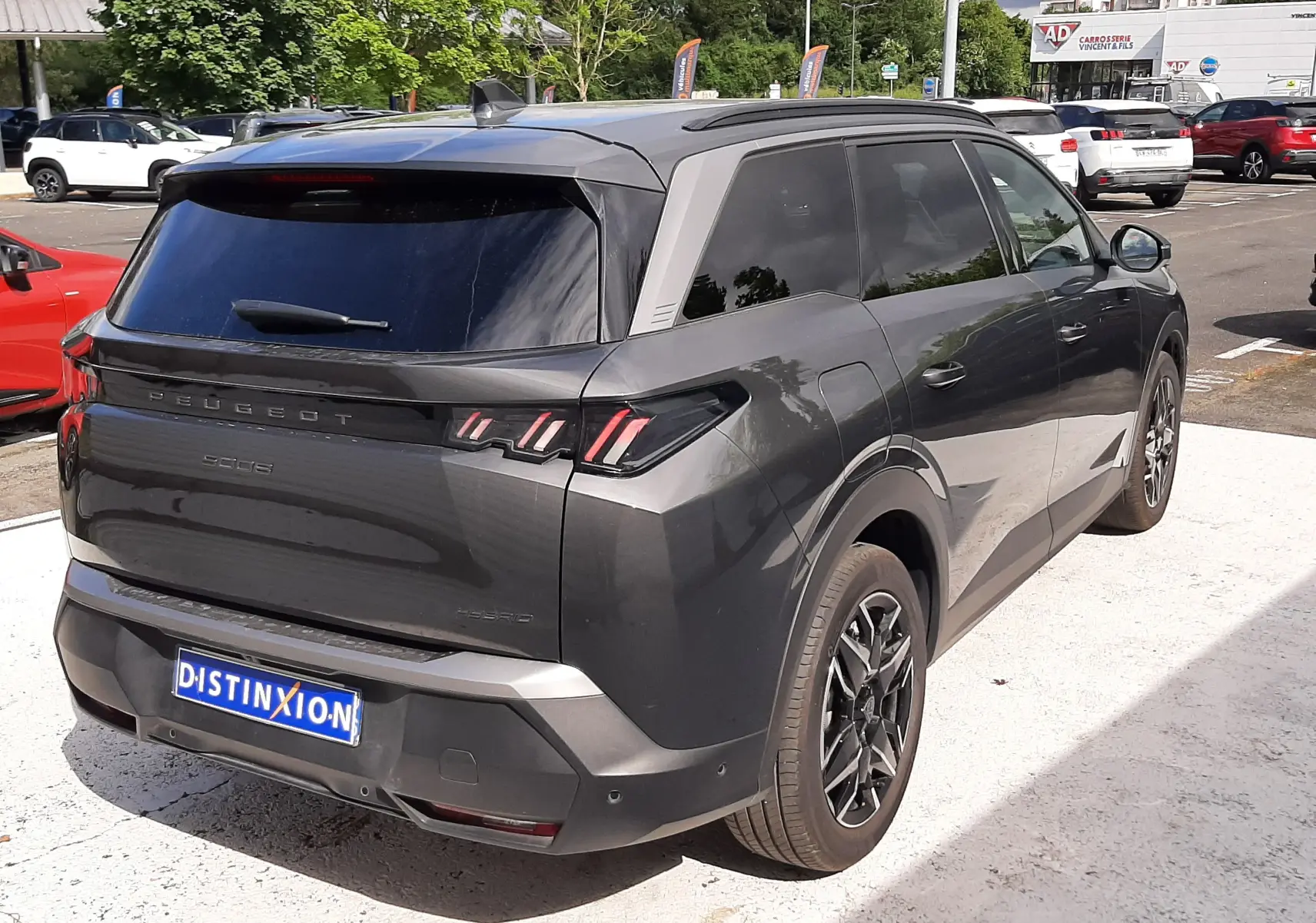 Vue 3/4 arrière droite du Peugeot 5008 Hybrid gris titane métal avec vitres teintées et jantes alliage noires.