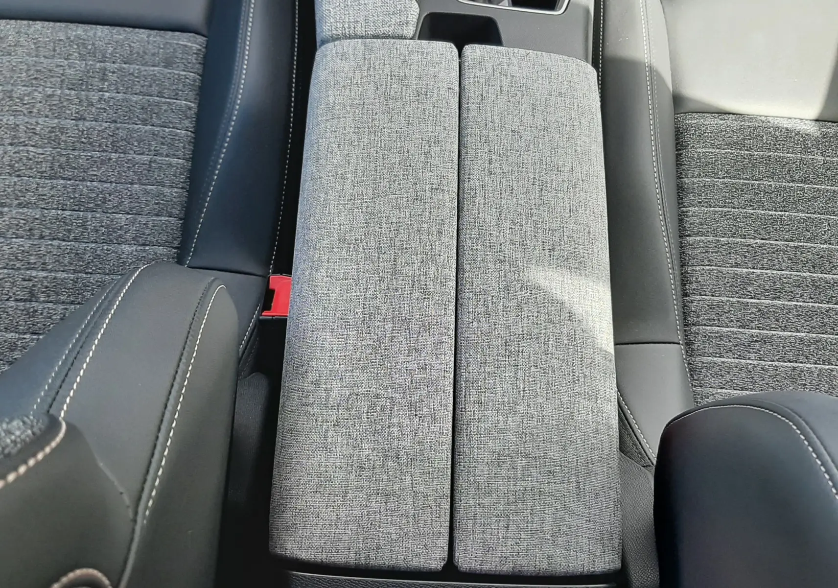Vue plongeante sur l'accoudoir central gris tissu et cuir noir entre les sièges avant du Peugeot 5008 Hybrid 2025.