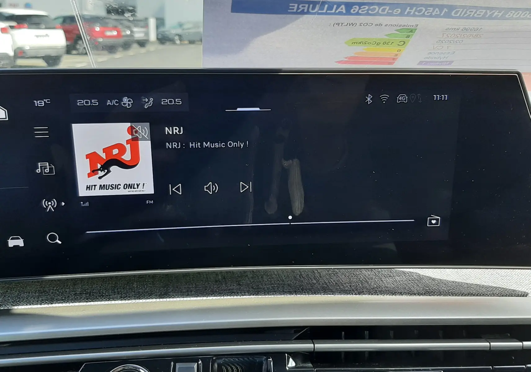 Vue intérieure du tableau de bord du Peugeot 5008 Hybrid 2025, écran tactile affichant la radio NRJ, avec bouton start/stop visible.