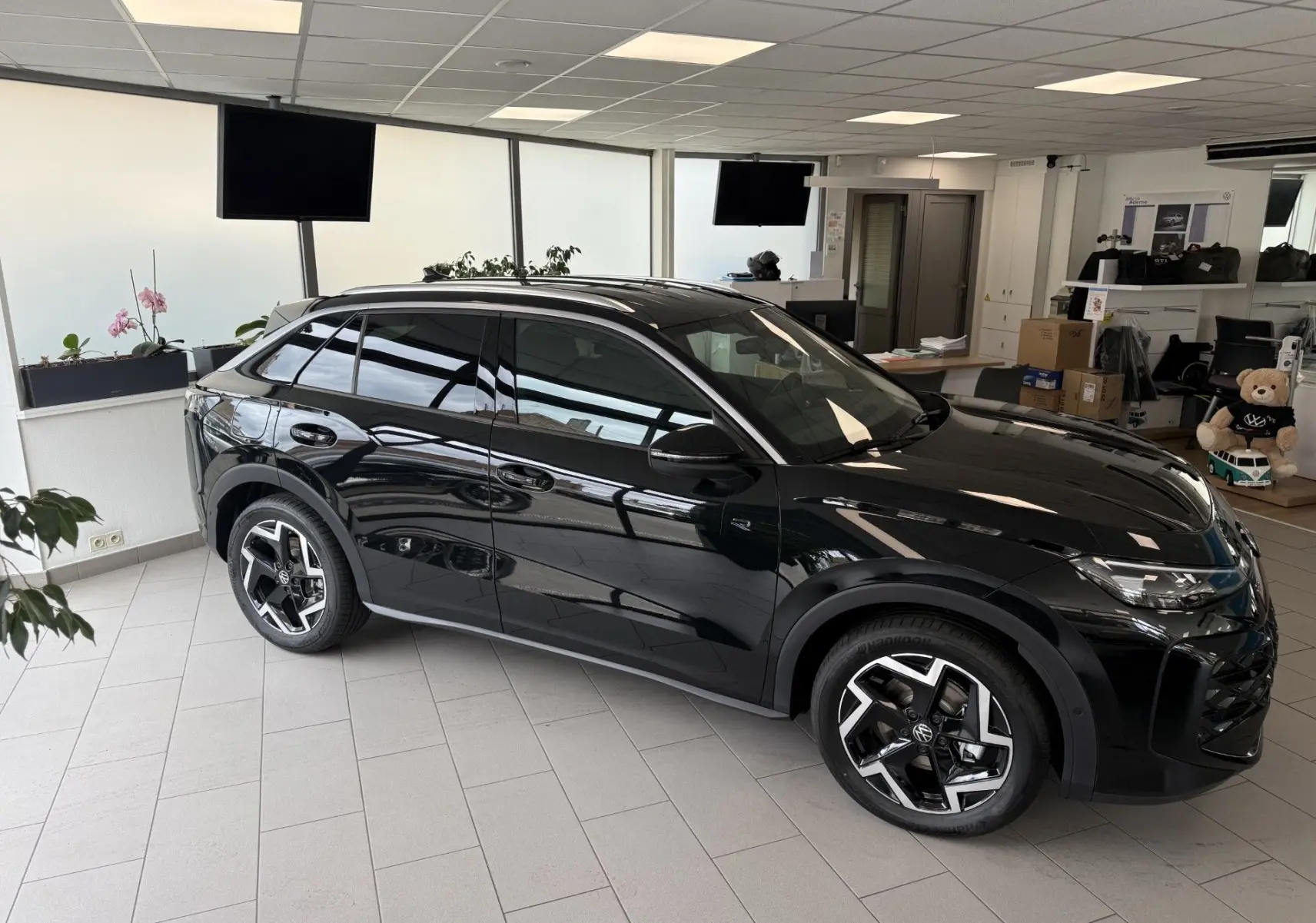Volkswagen T-Roc R-Line noir intense en vue 3/4 avant droit, avec jantes alliage et vitres teintées, dans un showroom.