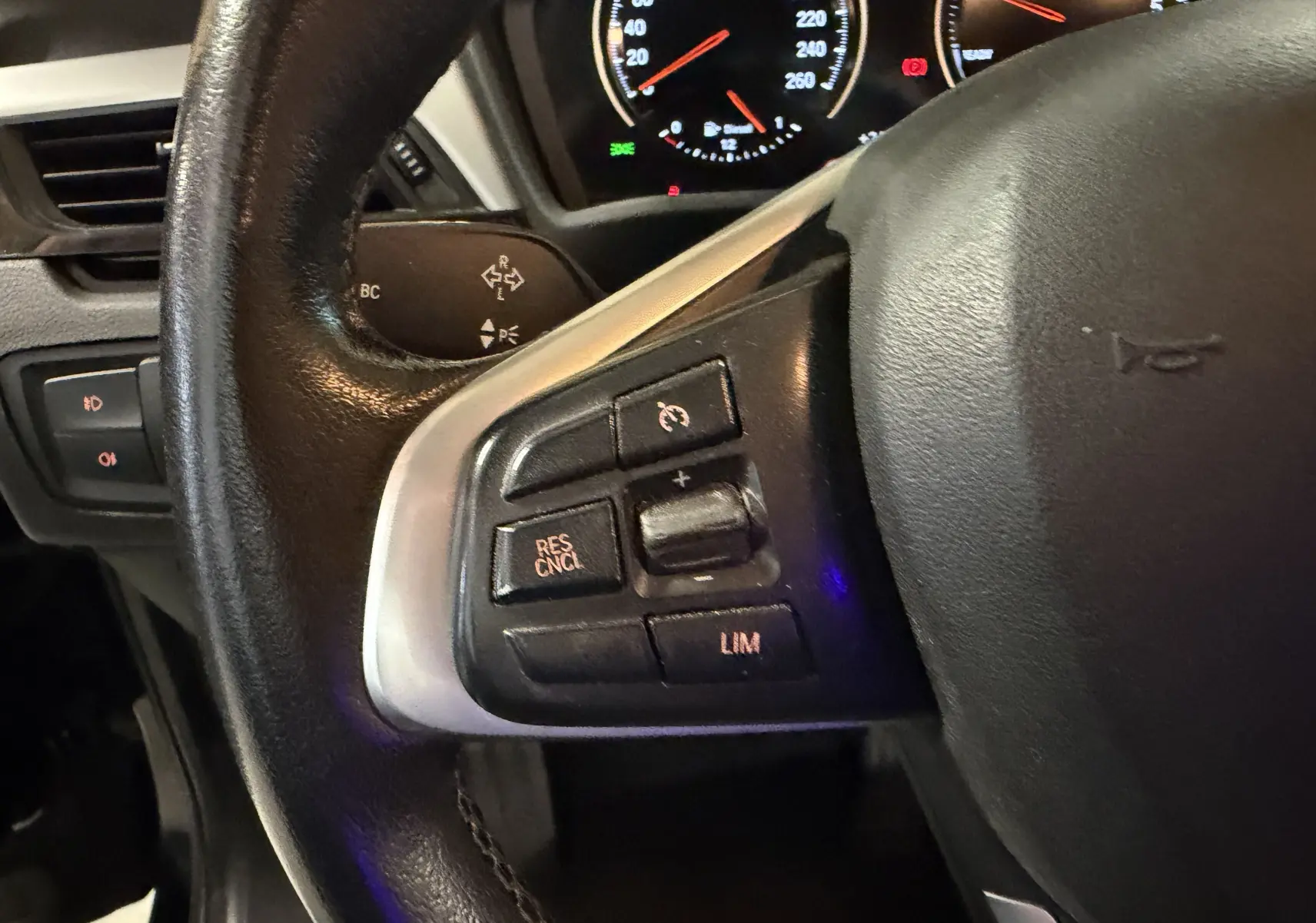 Gros plan sur le volant noir de la BMW X1 2019, avec commandes de régulateur de vitesse et tableau de bord éclairé en arrière-plan.