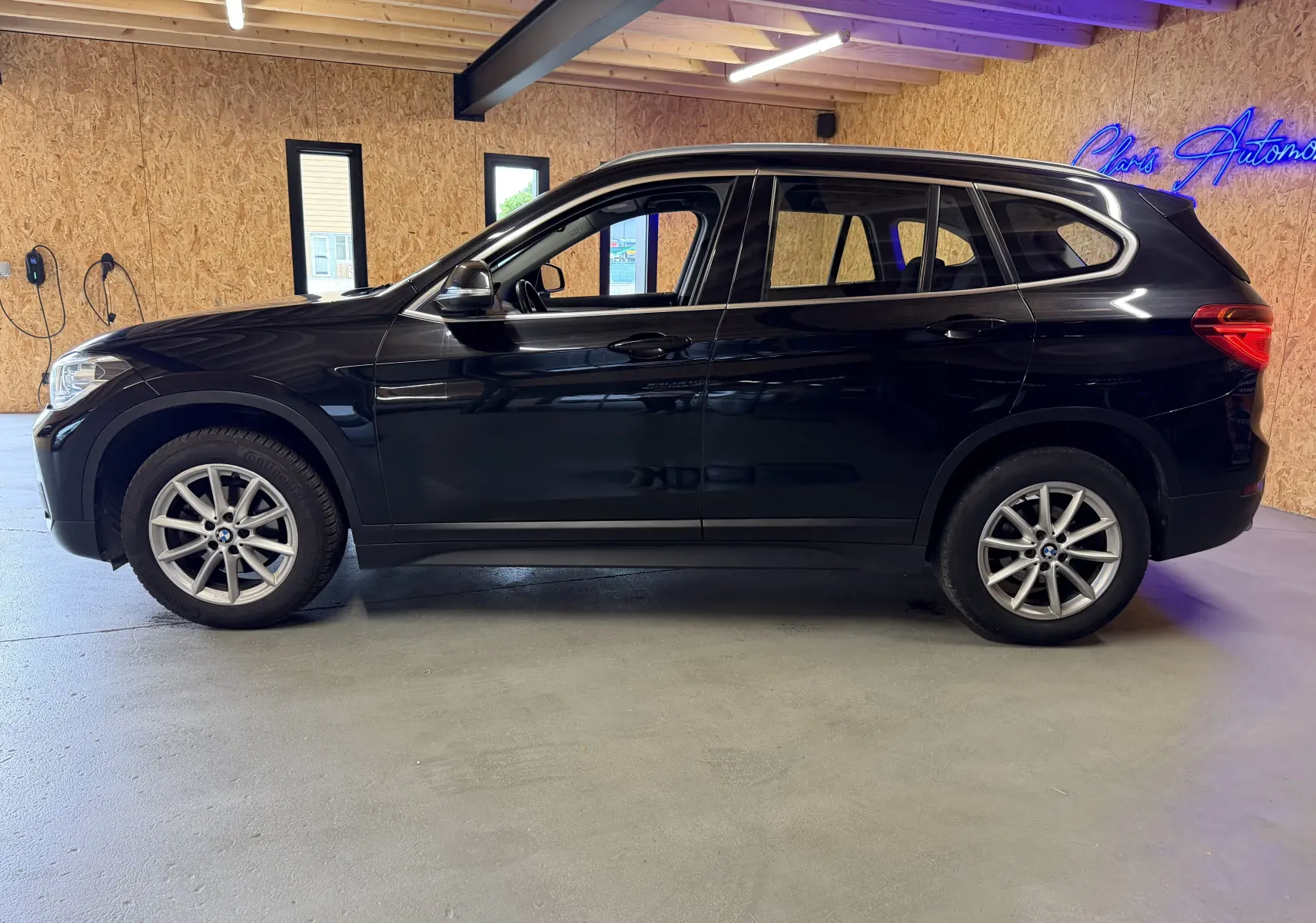 BMW X1 F48 noir vue de profil côté gauche, avec jantes alliage et intérieur visible en arrière-plan intérieur.