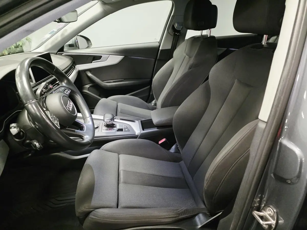 Vue intérieure côté gauche de l'Audi A4 Avant gris, montrant les sièges avant en tissu et le volant multifonction cuir.