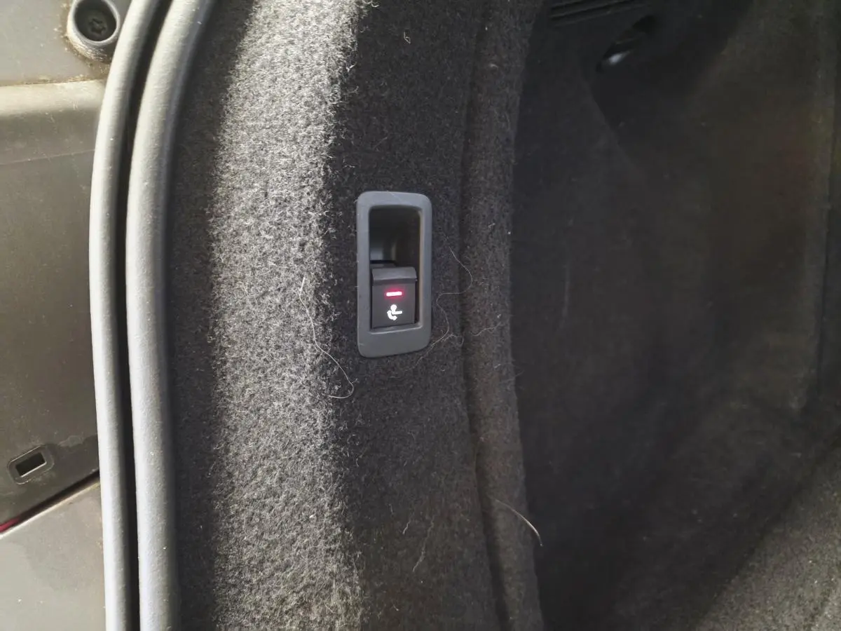 Gros plan sur le bouton de rabattement électrique des sièges dans le coffre de l'Audi A4 Avant gris.