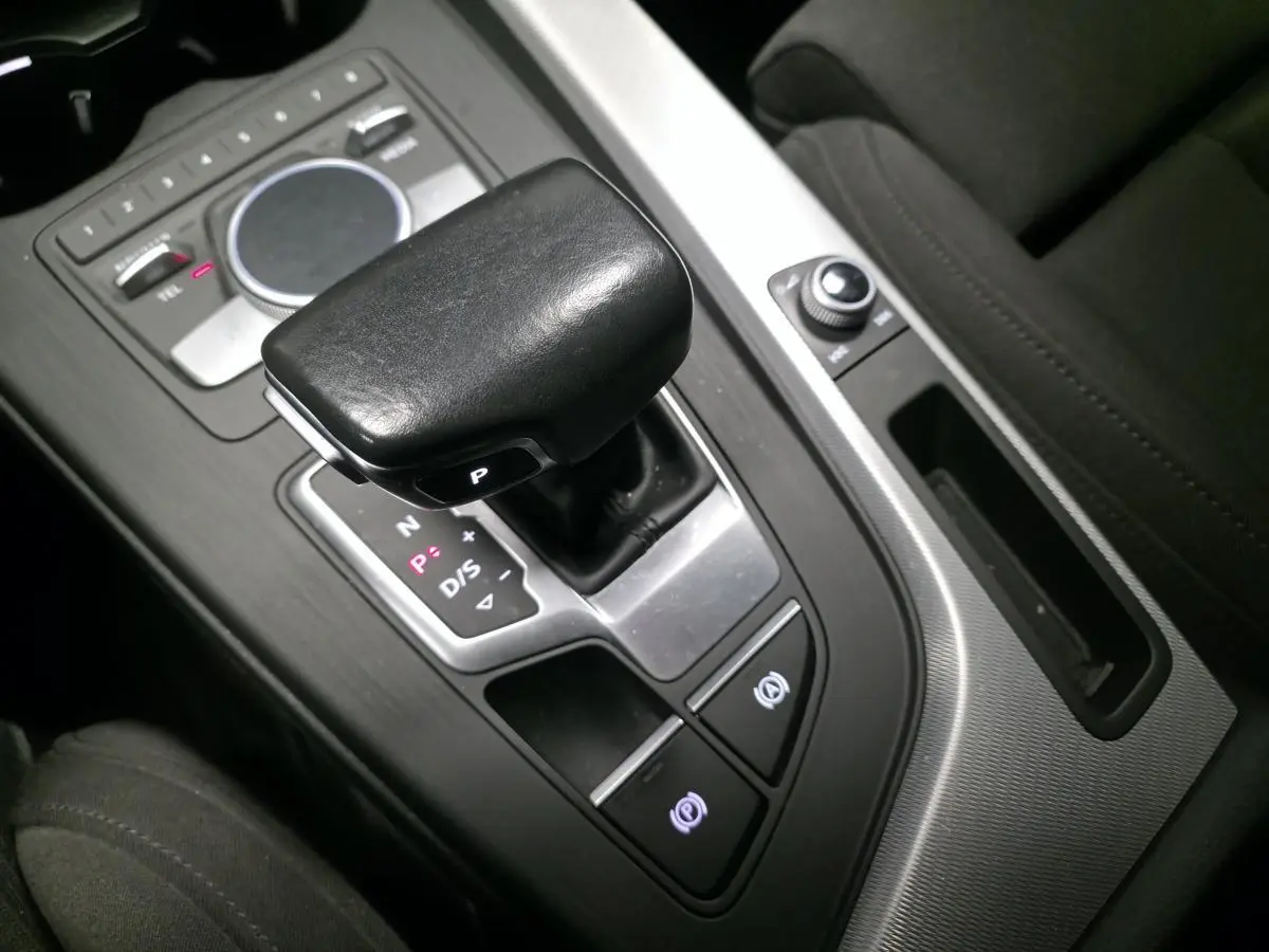 Gros plan sur le levier de vitesses automatique noir et la console centrale aluminium d'une Audi A4 Avant gris, intérieur tissu noir.