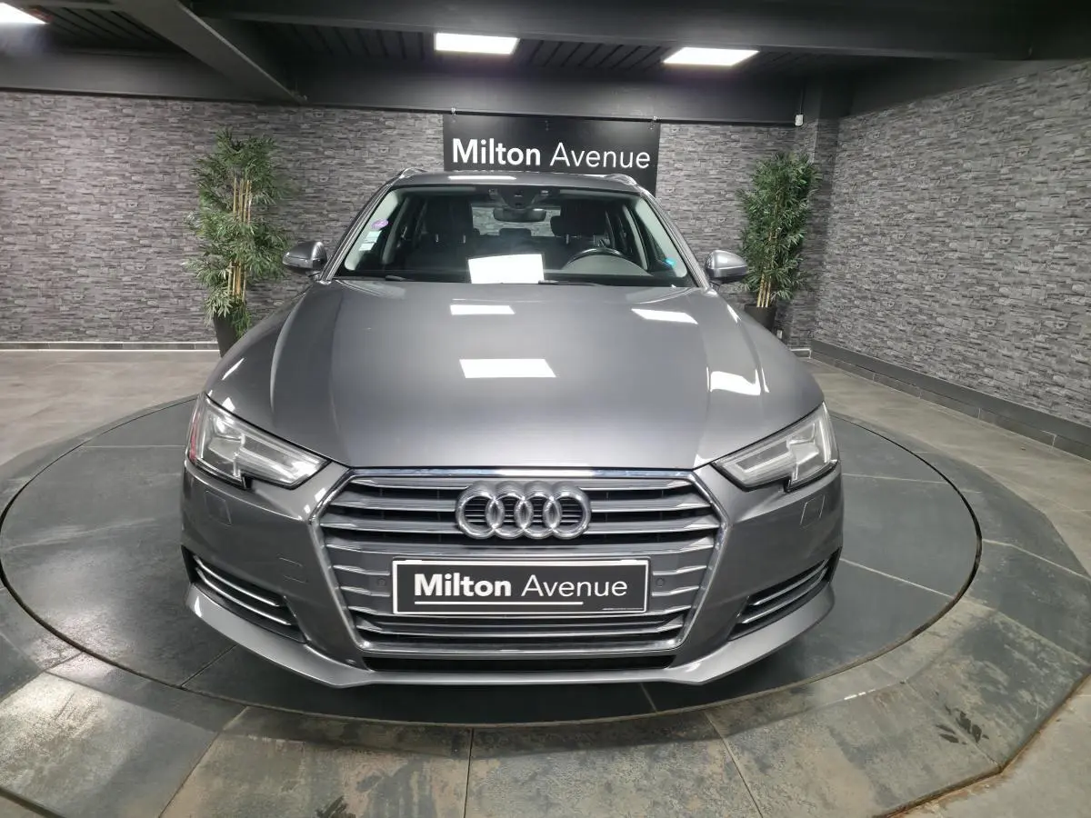 Vue frontale d'une Audi A4 Avant 2.0 TFSI Ultra gris métallisé avec calandre hexagonale et phares LED dans un showroom.