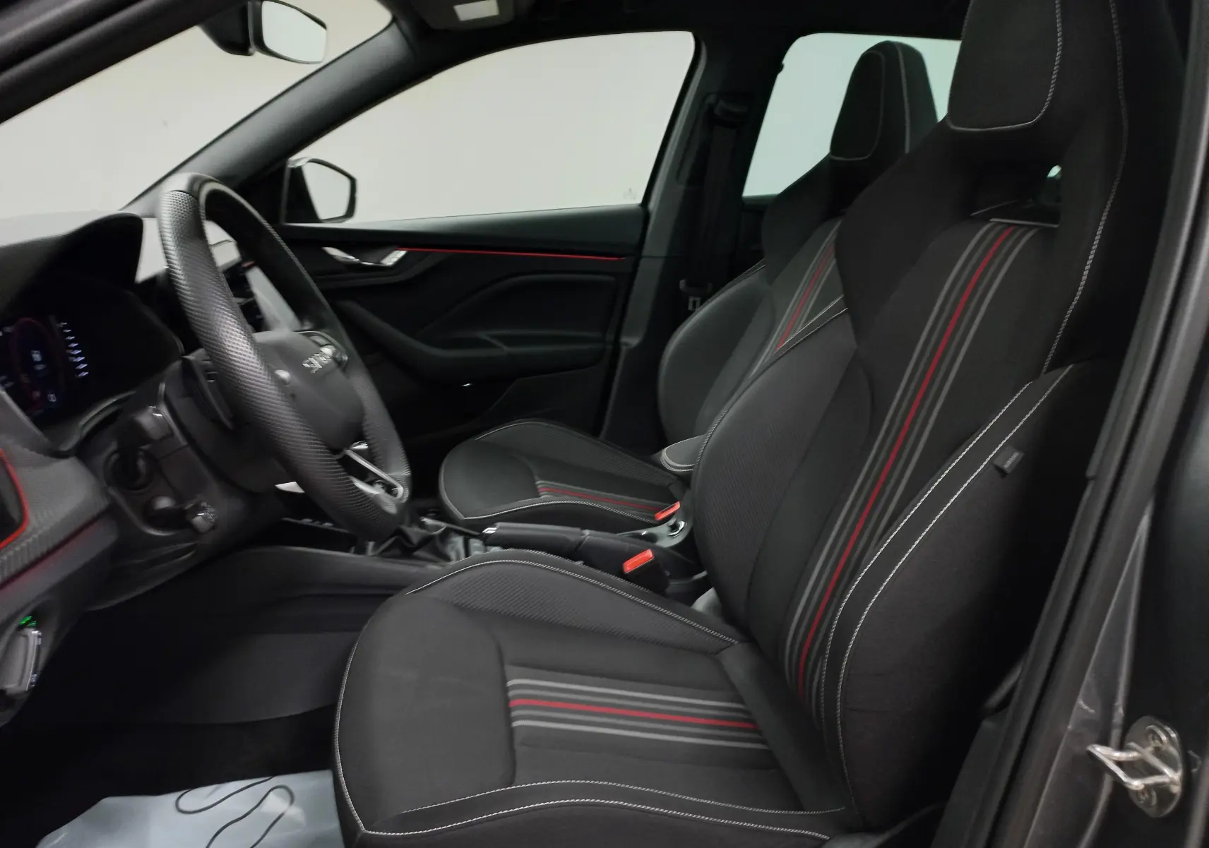 Vue intérieure côté conducteur de la Skoda Scala Monte-Carlo 2025 avec sièges noirs à surpiqûres rouges et blanches.