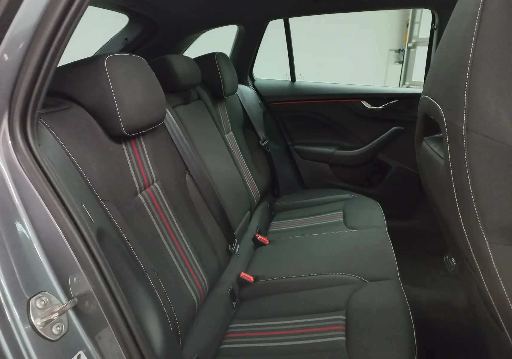 Vue côté gauche de l'habitacle arrière de la Skoda Scala 2025 gris graphite avec sièges noirs à bandes rouges et grises.