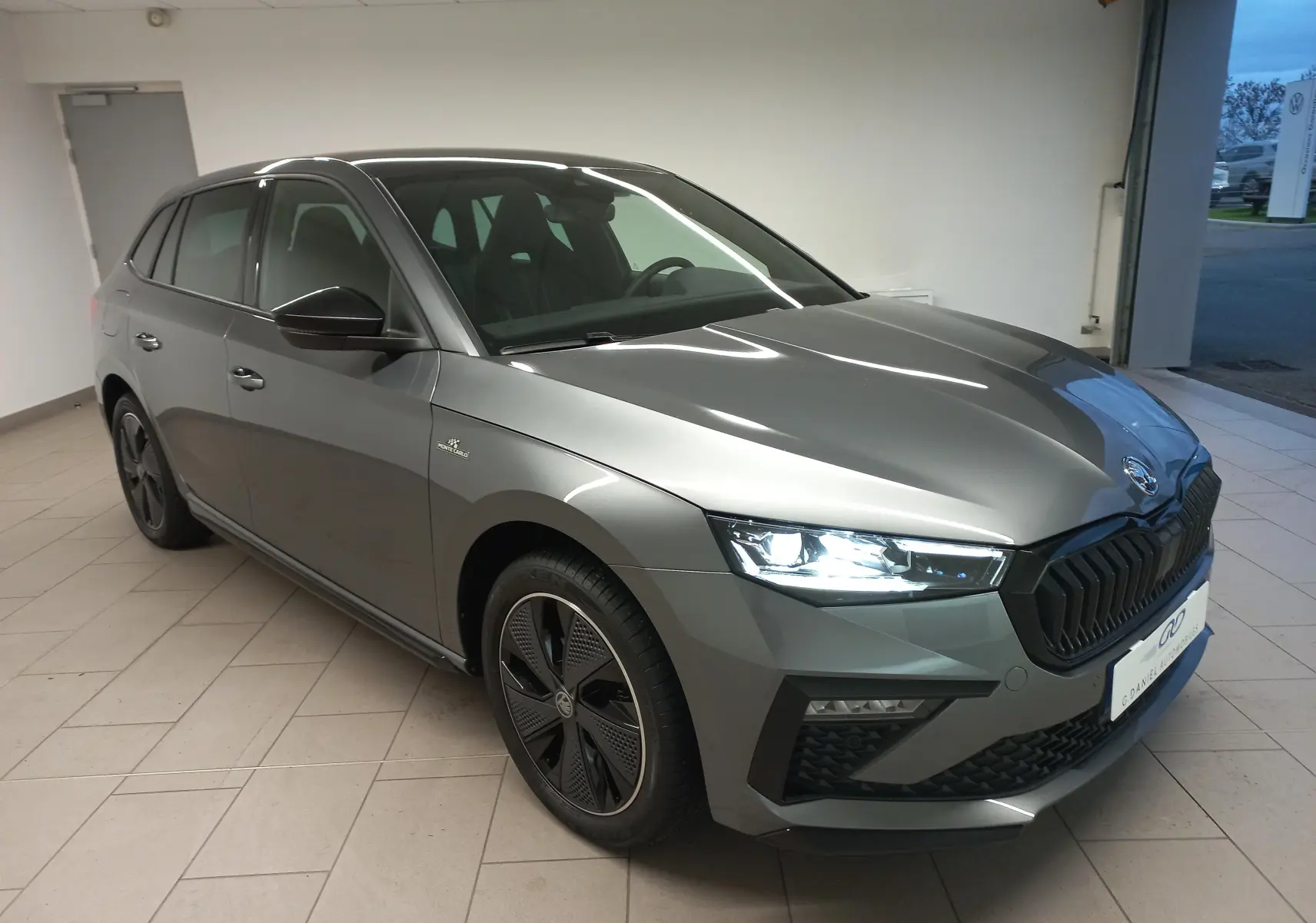 Vue 3/4 avant droite d'une Skoda Scala 2025 gris graphite avec phares allumés et jantes spécifiques Monte-Carlo.