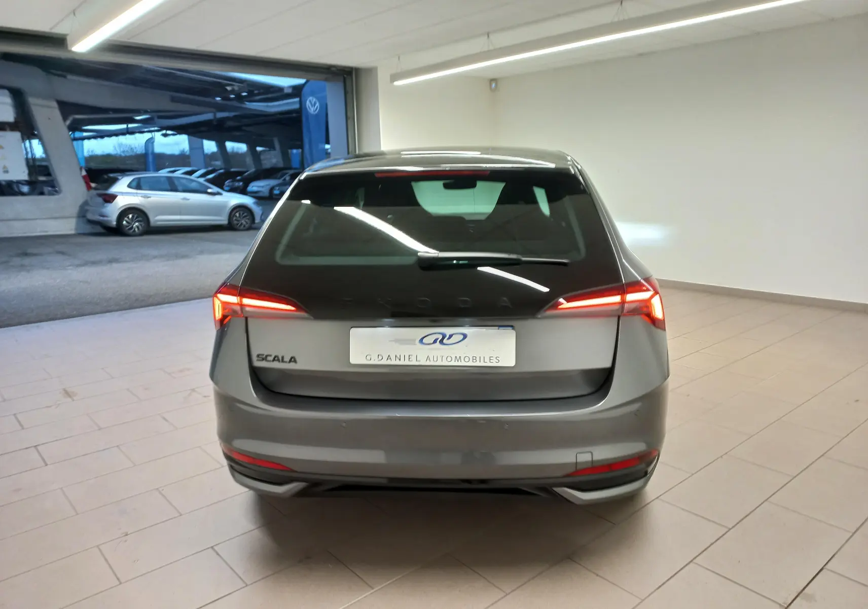 Vue arrière d'une Skoda Scala 2025 gris graphite avec feux LED allumés dans un showroom lumineux.